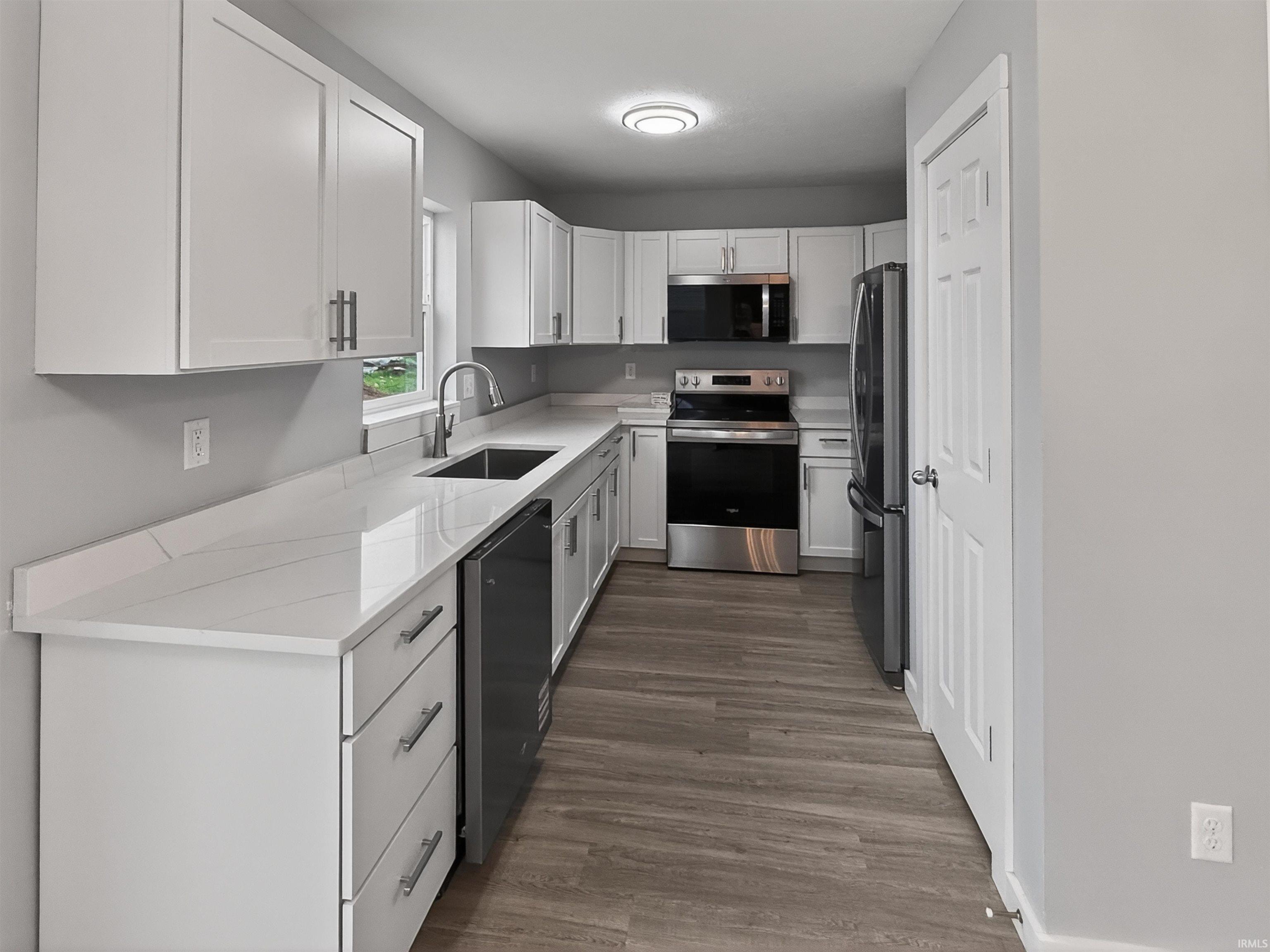 Contemporary kitchen featuring white shaker cabinetry, stainless steel appliances, light-toned countertops, a stainless steel undermount sink, and wood-finish flooring