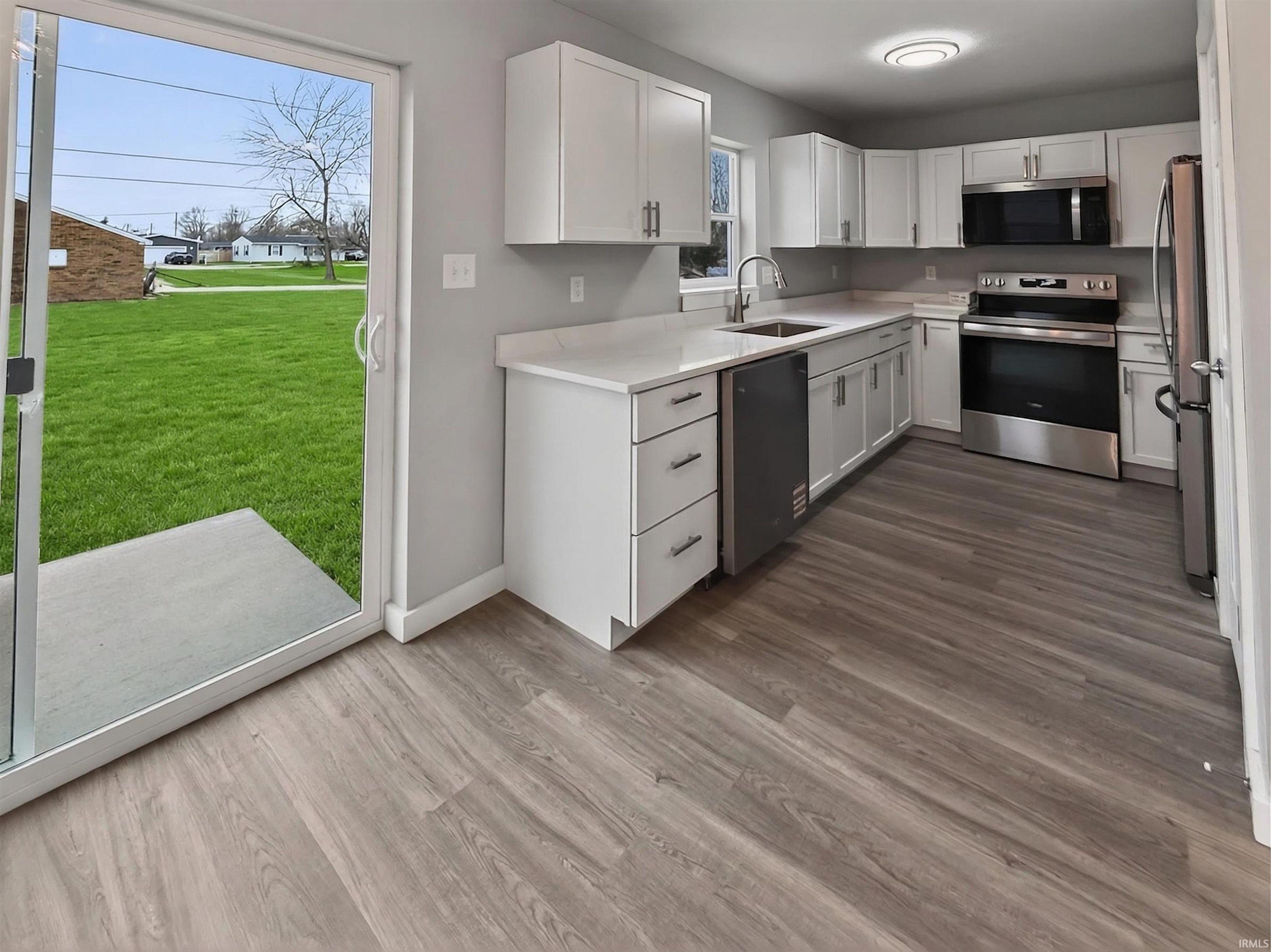 Modern kitchen featuring white cabinetry, stainless steel appliances, light countertops, wood-finish flooring, and direct access to a rear patio and green space
