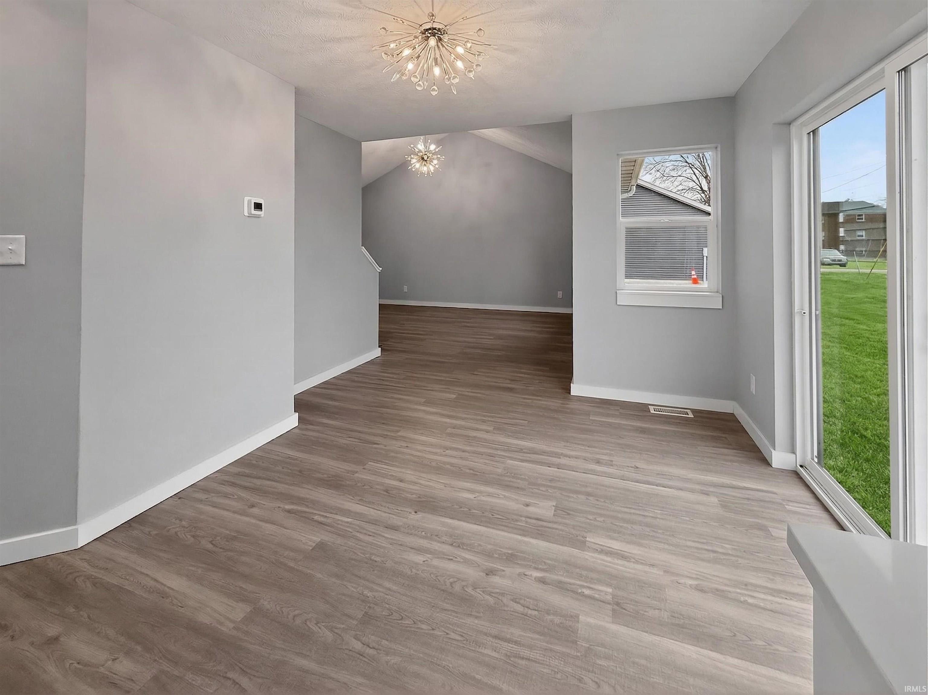 Spacious interior featuring wood-finish flooring, light grey wall paint, and a contemporary chandelier