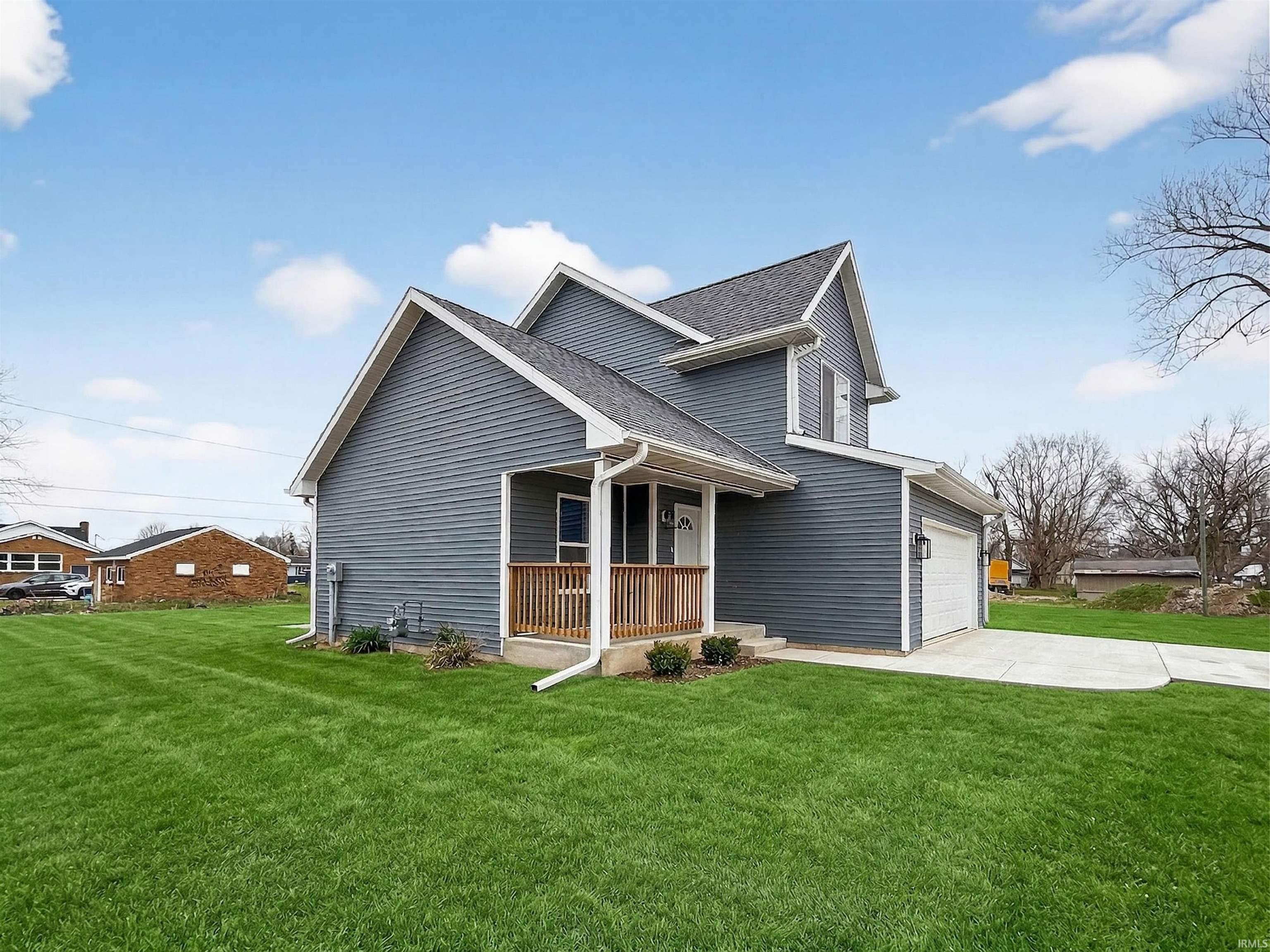 Two-story residence featuring blue vinyl siding, an attached garage, a covered front porch with wood railings, a concrete driveway, and a well-maintained lawn
