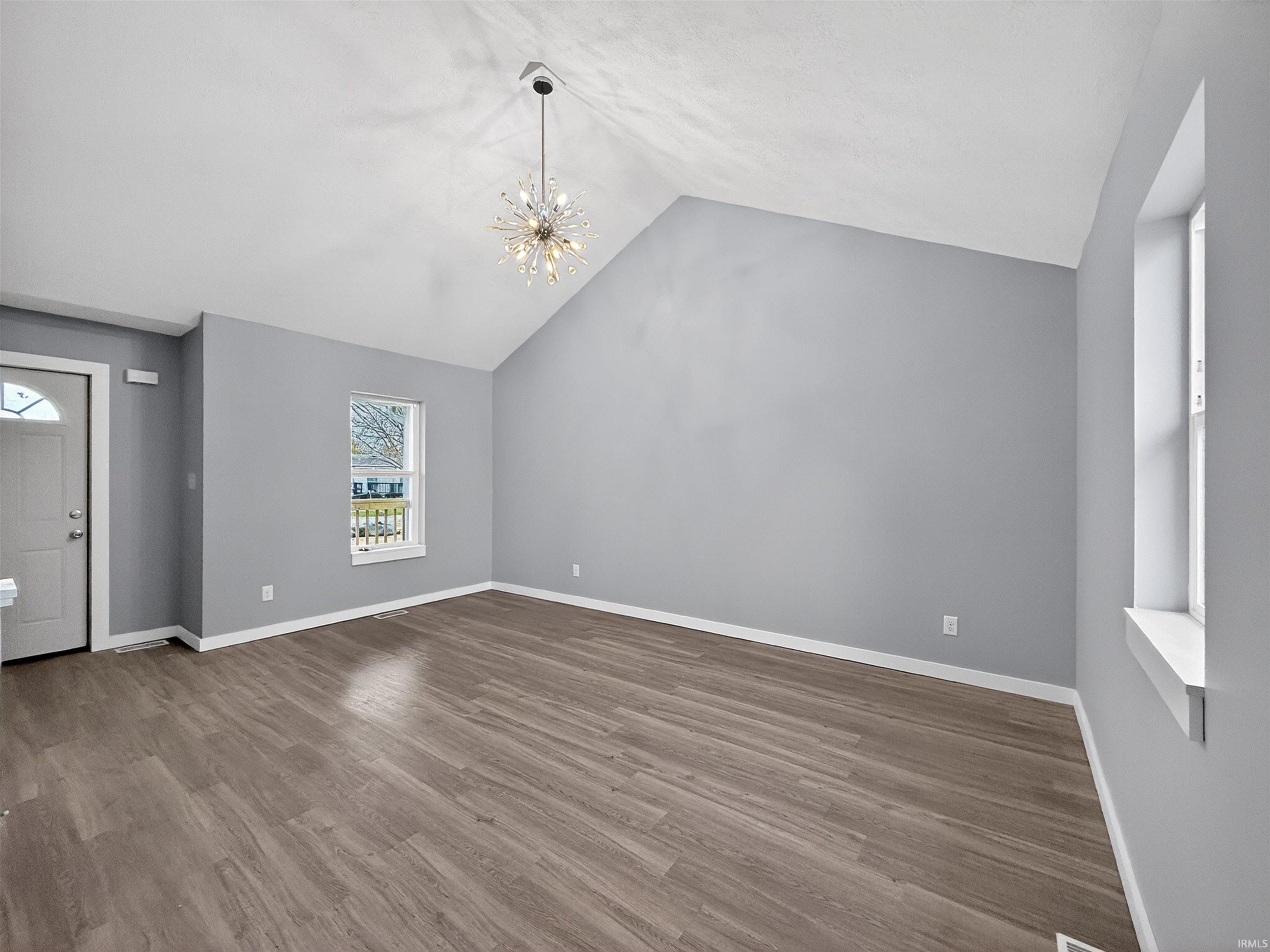 Spacious room featuring vaulted ceilings, wood-finish flooring, and a contemporary chandelier