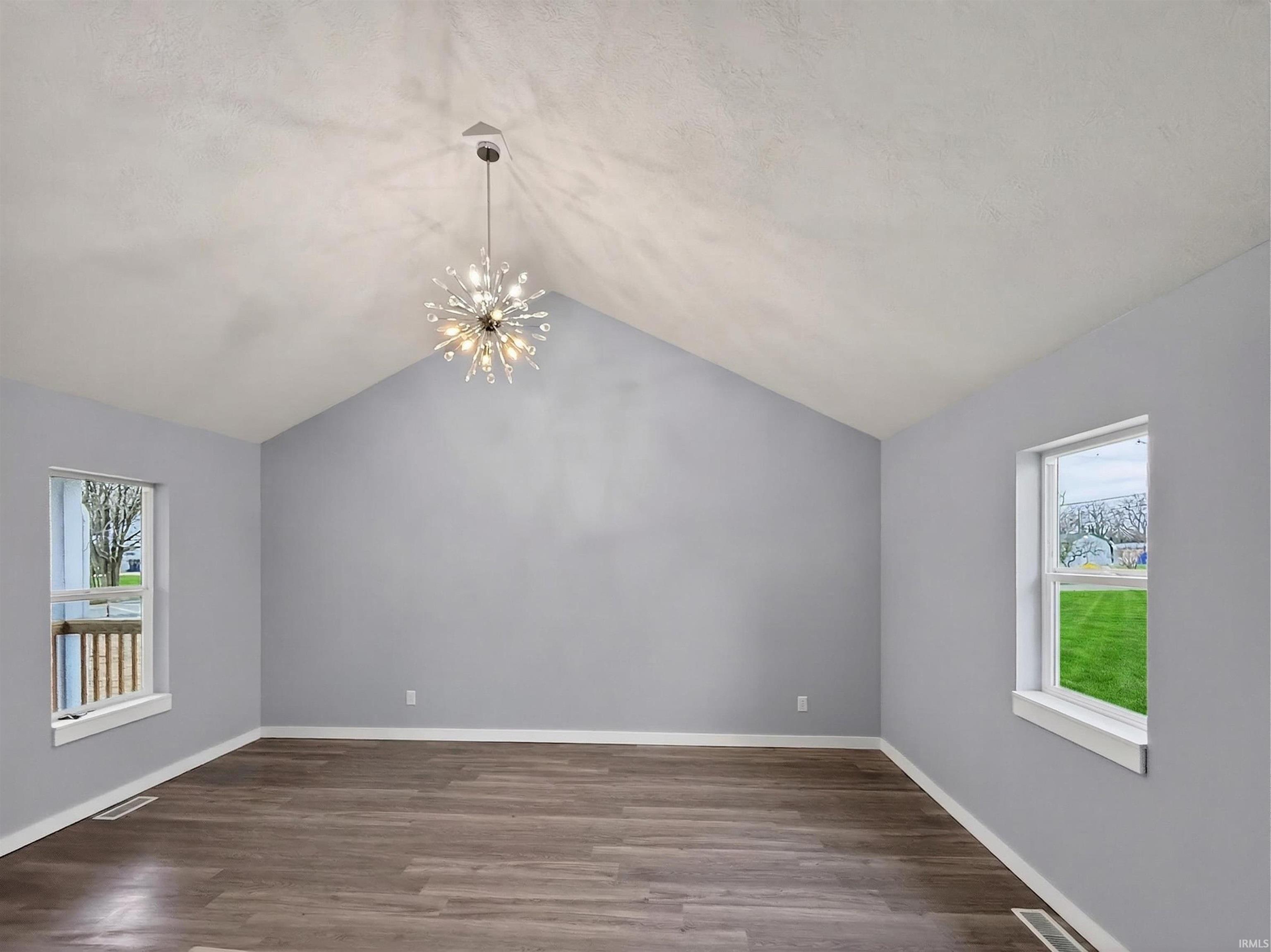 Room featuring a vaulted ceiling with a sputnik-style chandelier, wood-finish flooring, and white trim