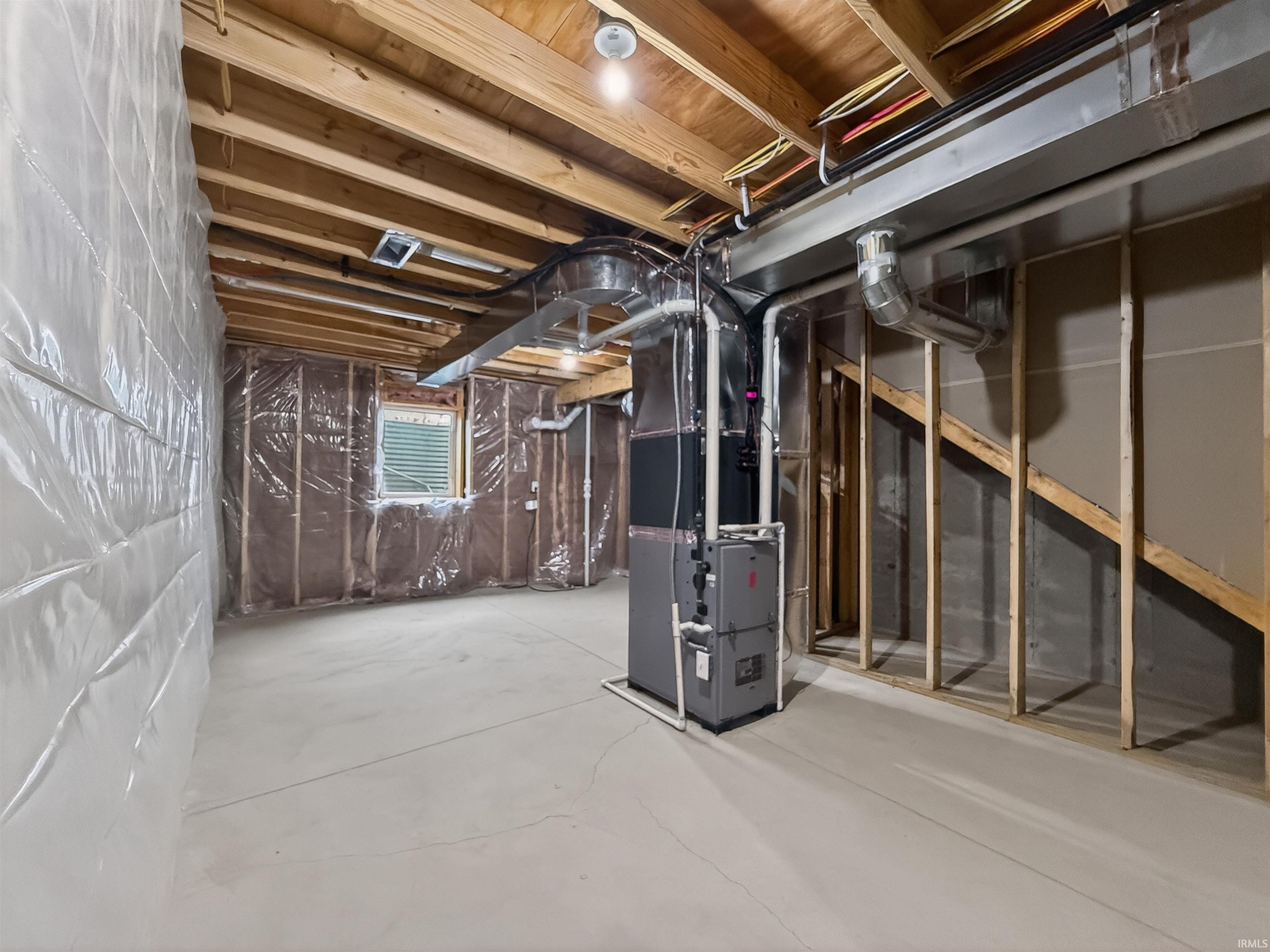 Unfinished basement space featuring exposed wooden ceiling joists, concrete flooring, and an existing HVAC system
