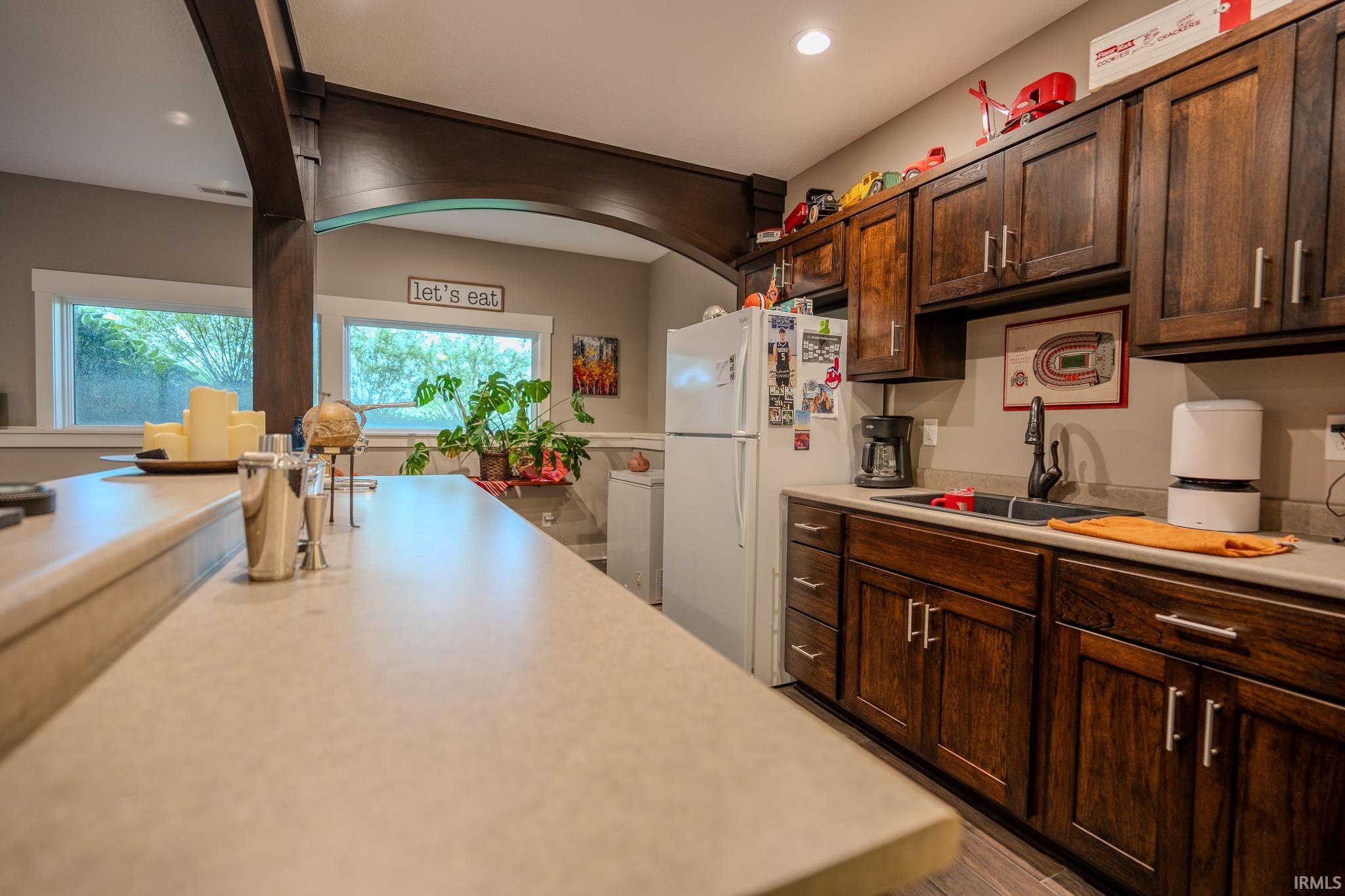 Kitchenette featuring dark wood cabinetry, a light-toned countertop, and a stainless steel sink with a dark faucet
