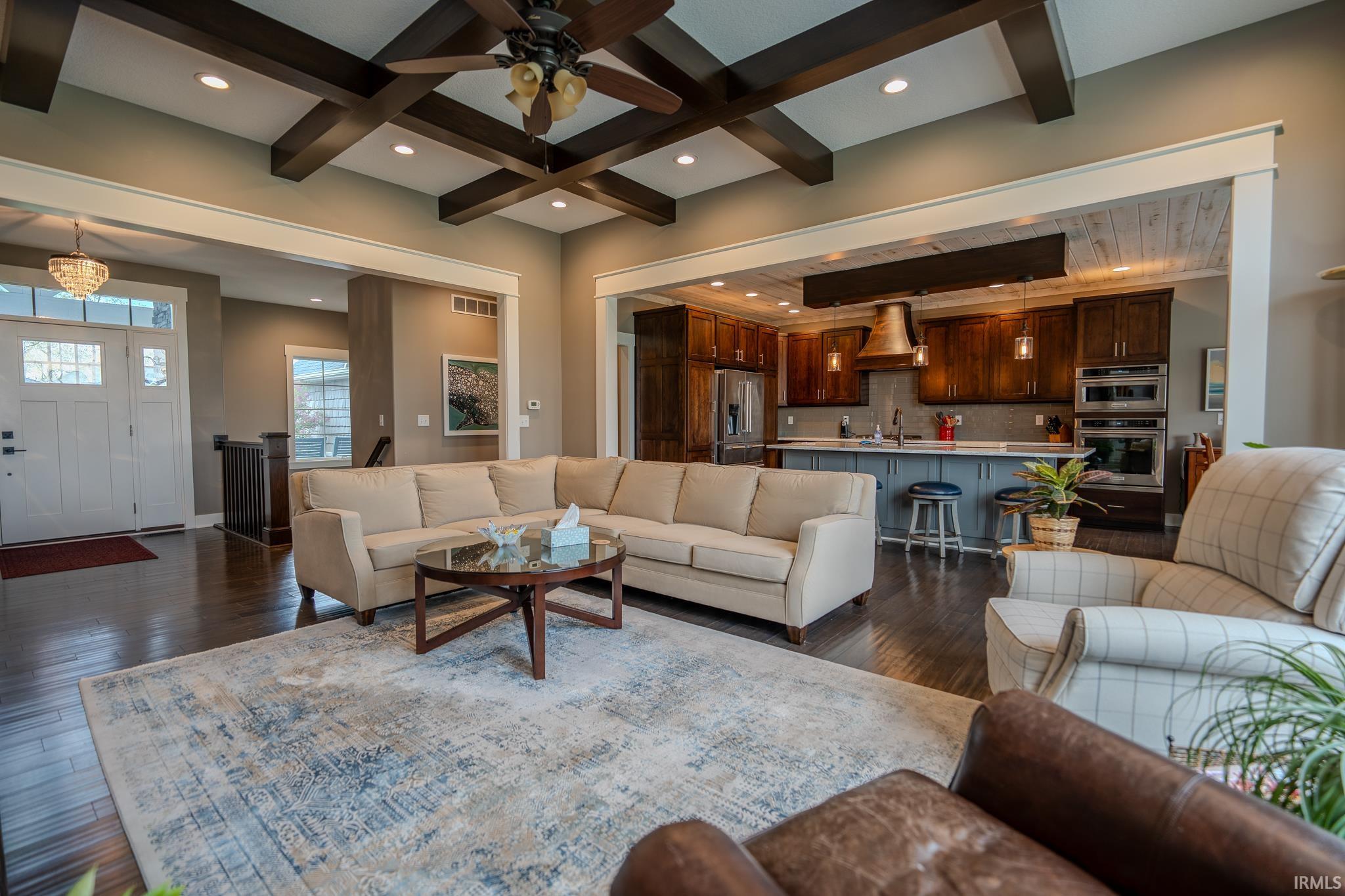 Spacious living area featuring coffered ceilings, wood-finish flooring, and an open concept layout to the kitchen
