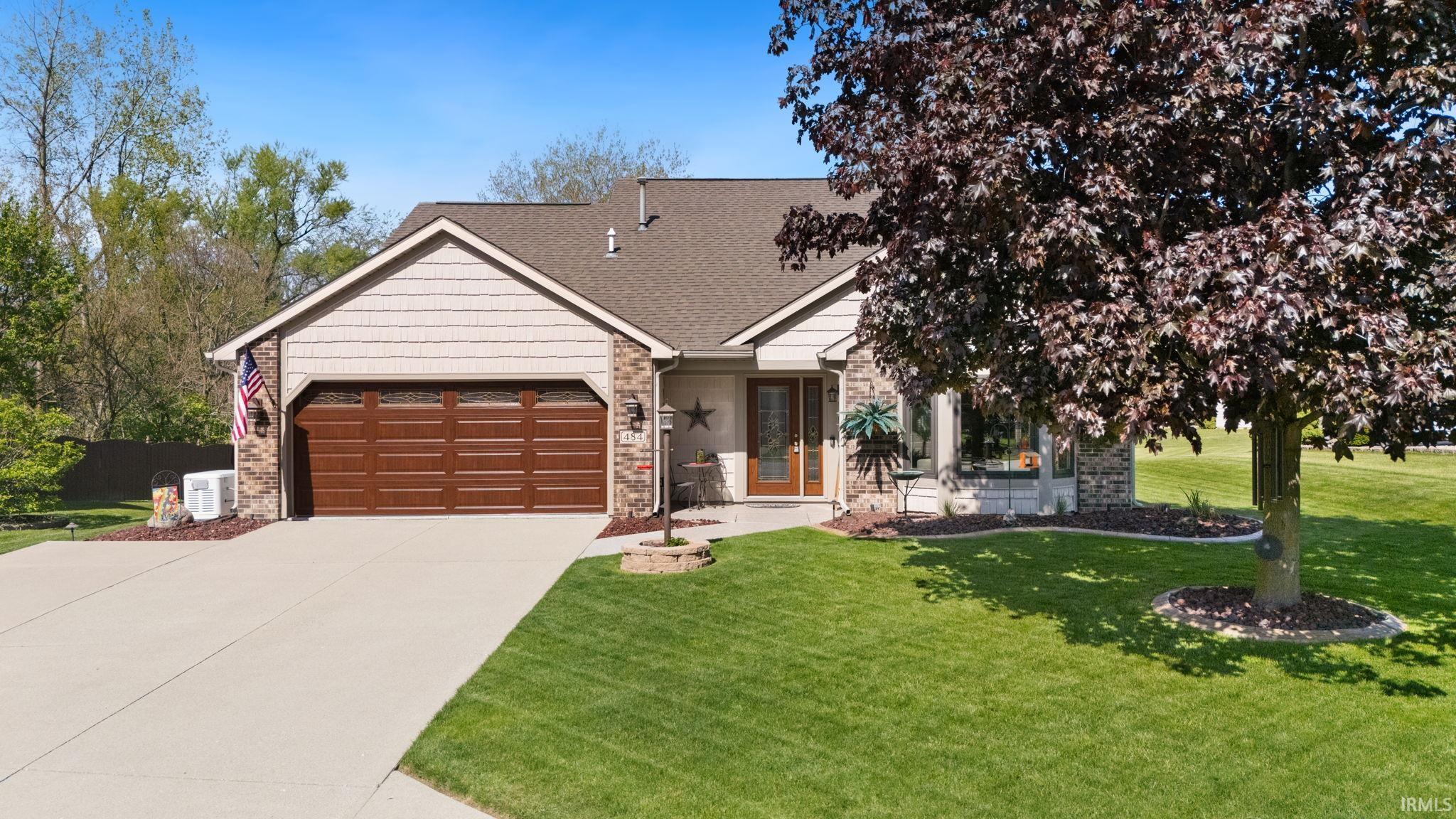 Exterior featuring a large driveway, attached garage with a decorative door, stone façade accents, and a prominent front yard tree