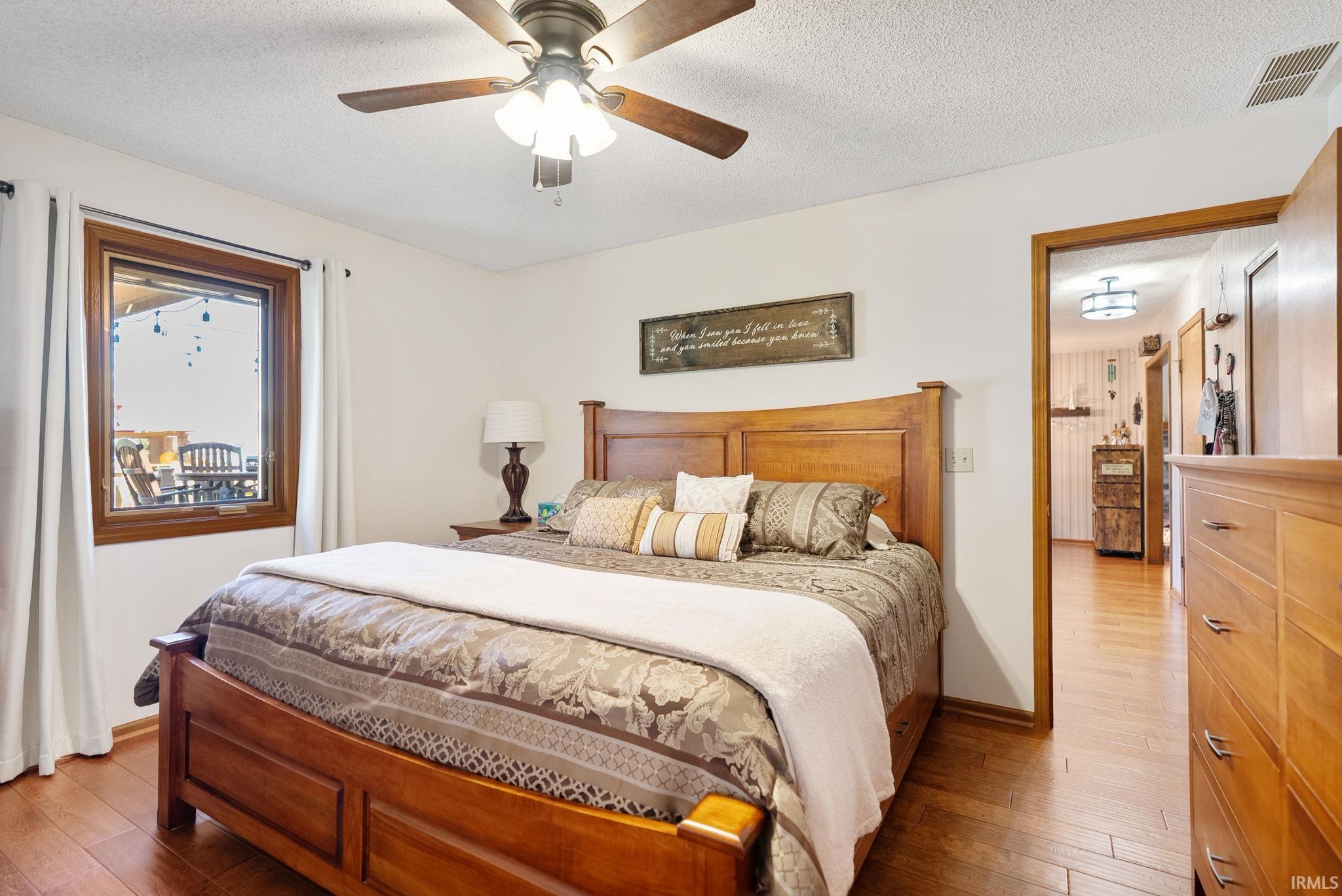 Spacious room featuring wood-finish flooring, a ceiling fan with integrated lighting, and a wood-framed window