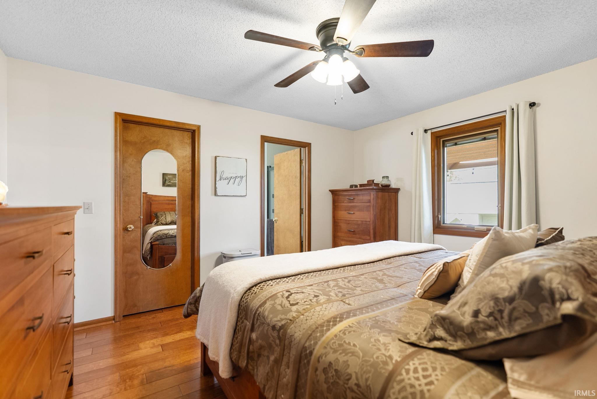 Bedroom featuring wood-finish flooring, a ceiling fan with light fixture, and a window with wood trim