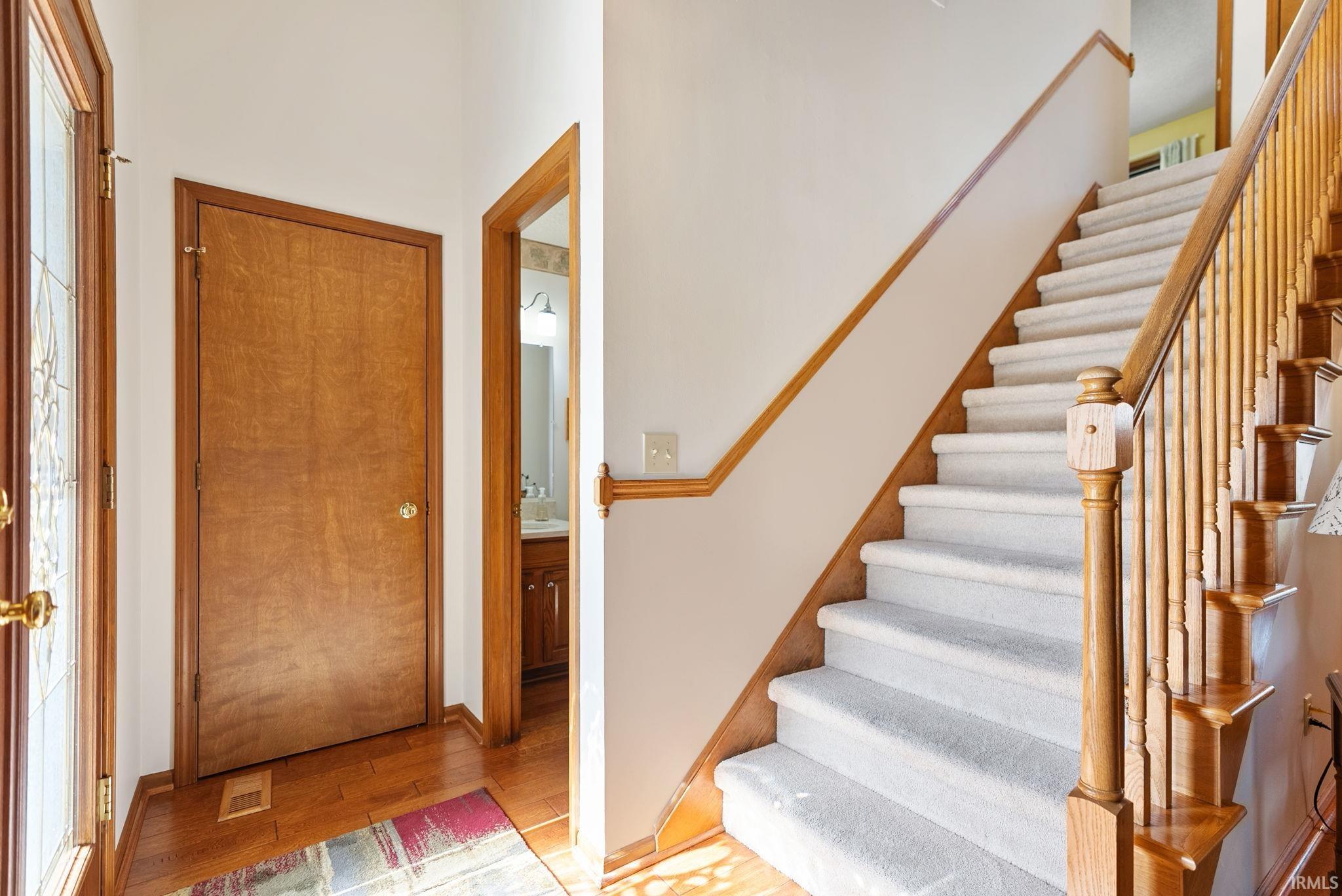 Entryway featuring a wood-finish door, wood-finish flooring, and a carpeted staircase with a wood-finish banister