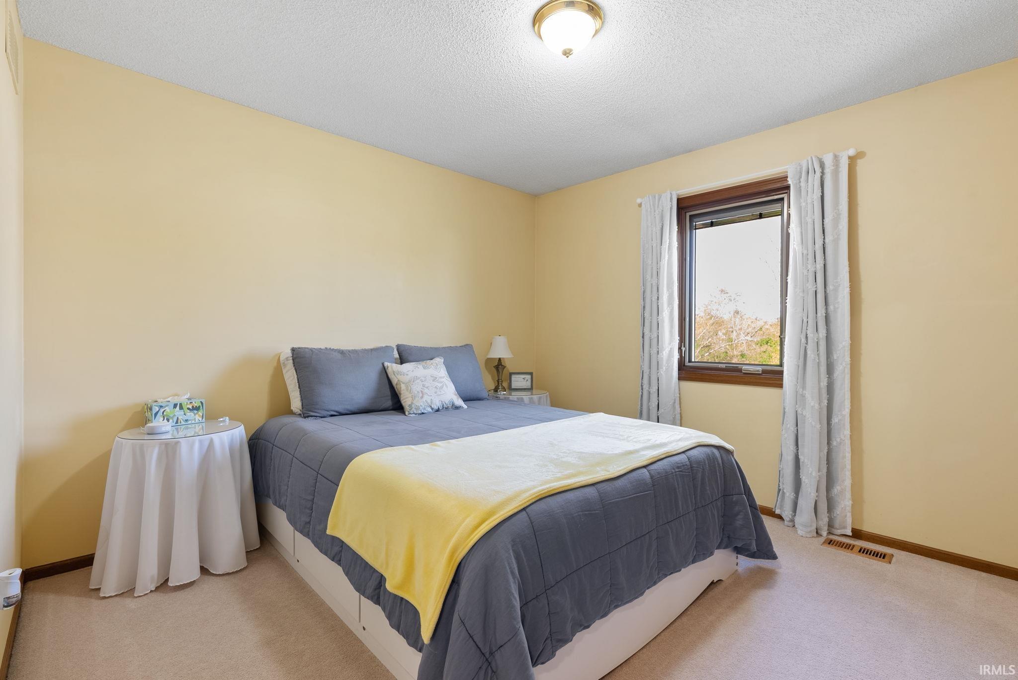 Bedroom featuring light cream-colored carpeting, warm yellow wall tones, and a single window with dark wood trim