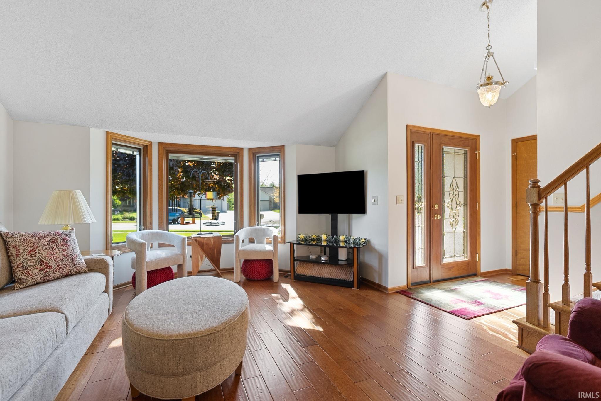Warm wood-finish flooring extends throughout this expansive living area, featuring a bay window with natural wood trim