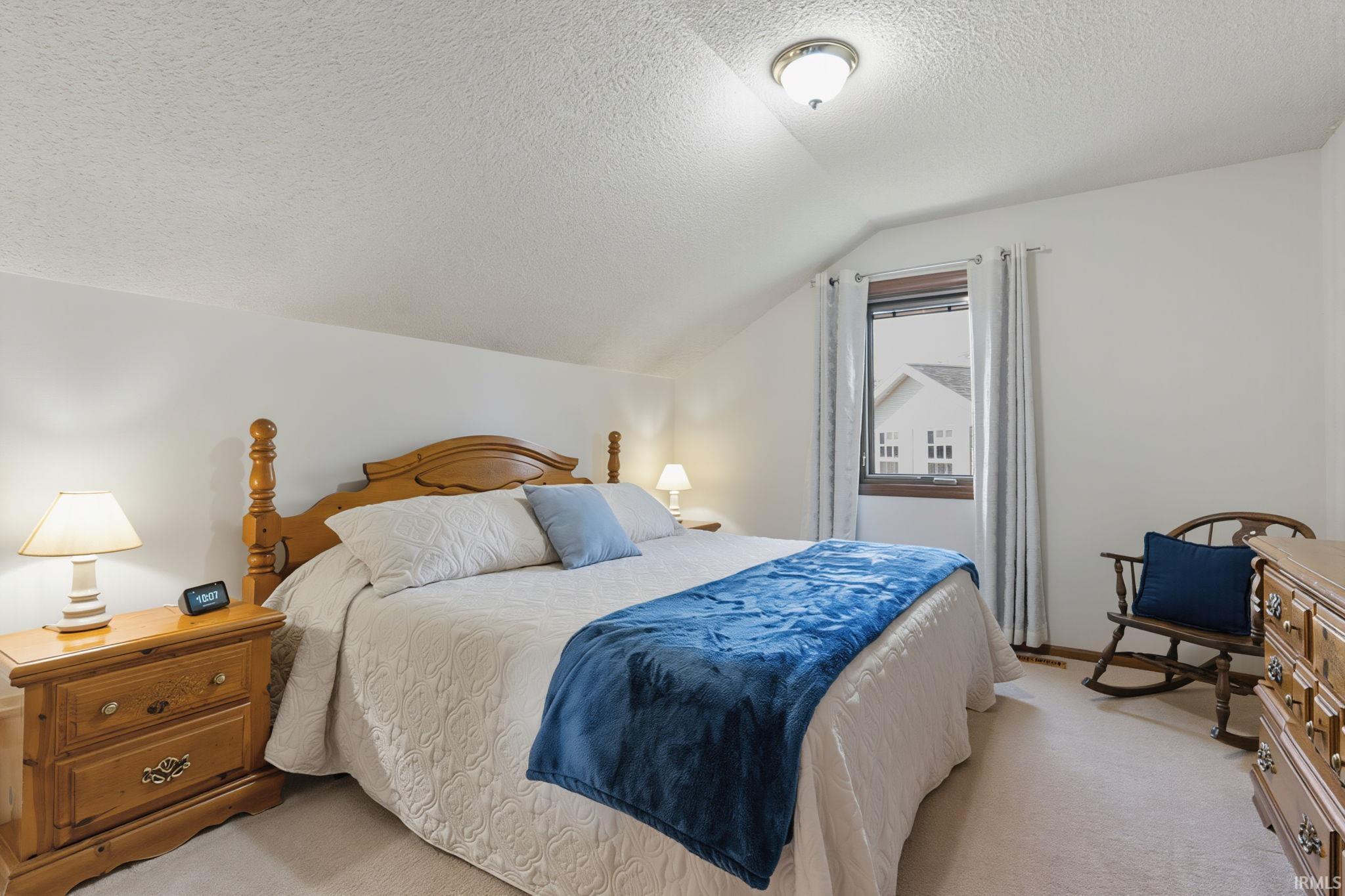 Bedroom featuring a sloped ceiling, light-colored carpet, and a window with wood trim