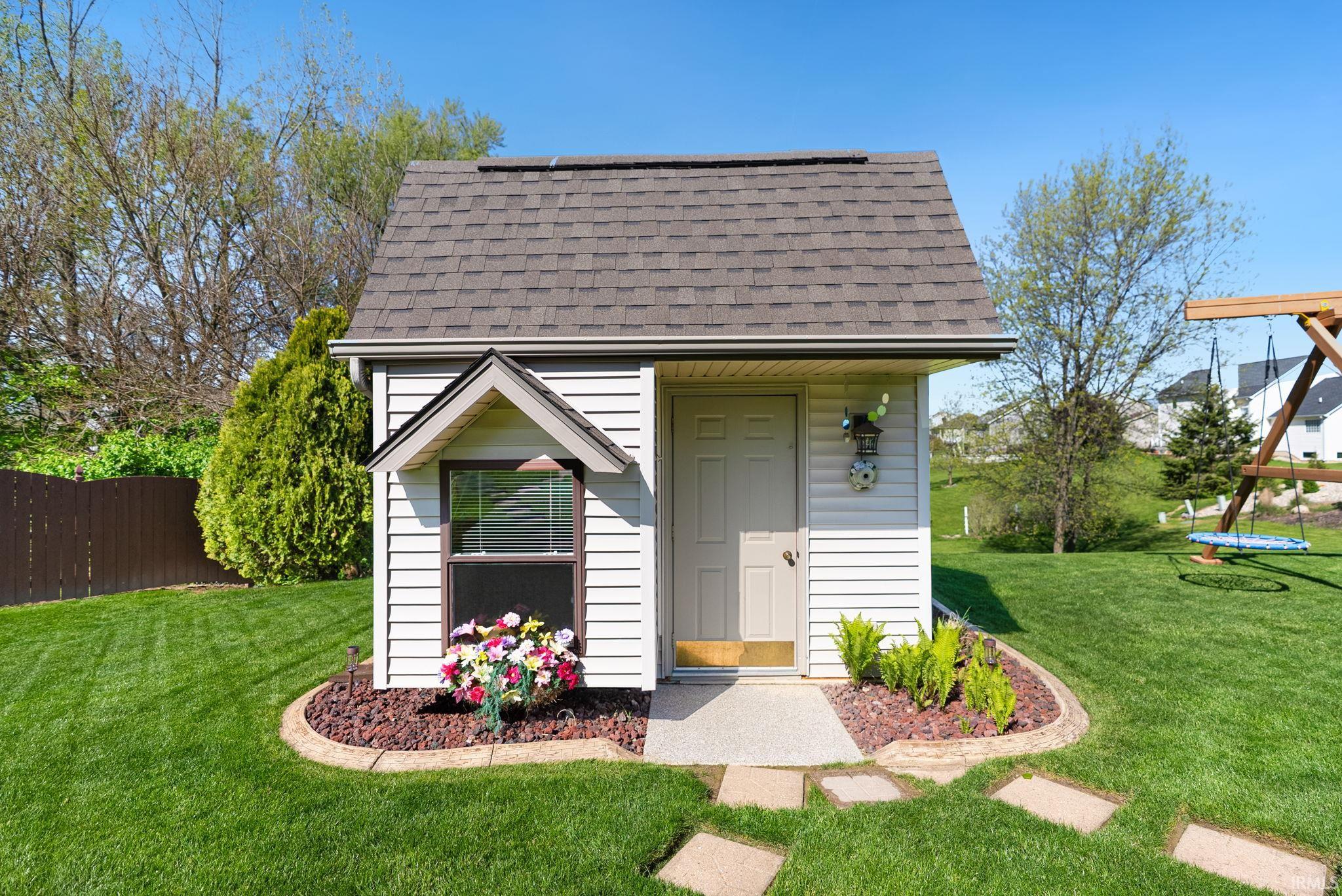 Detached storage shed featuring white siding, a shingled roof, a single window, and a door