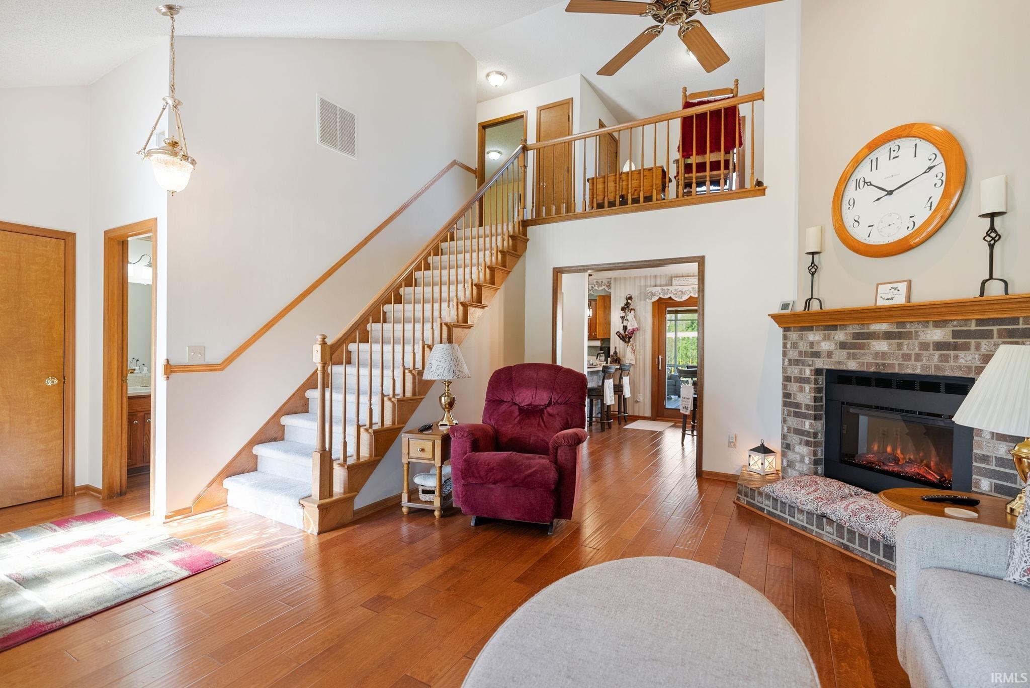 Two-story living area featuring wood-finish flooring, a brick-surround fireplace with a wood mantle, and a carpeted staircase with wood railings