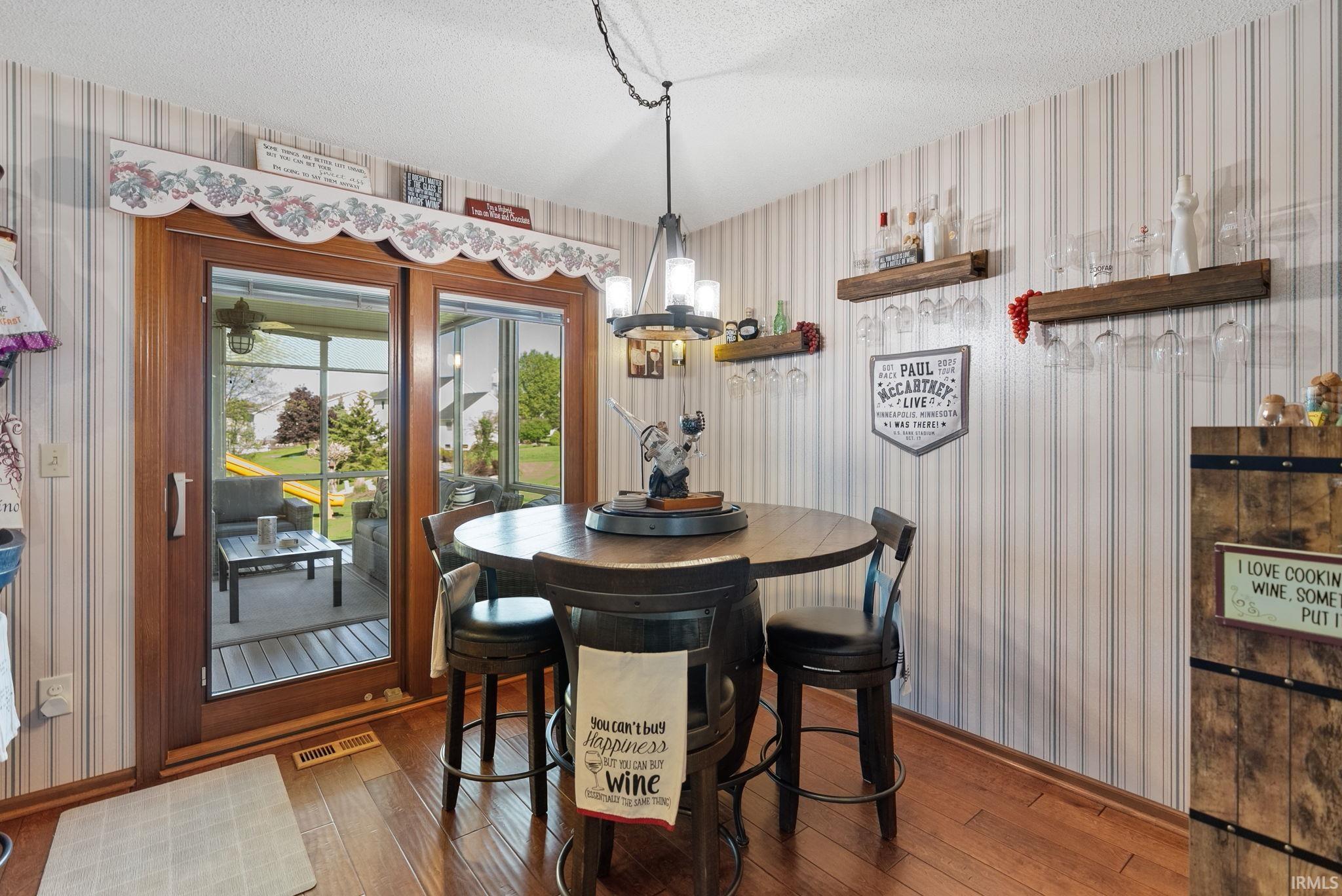 Dining area featuring wood-finish flooring, vertical striped wallpaper, and a multi-light chandelier