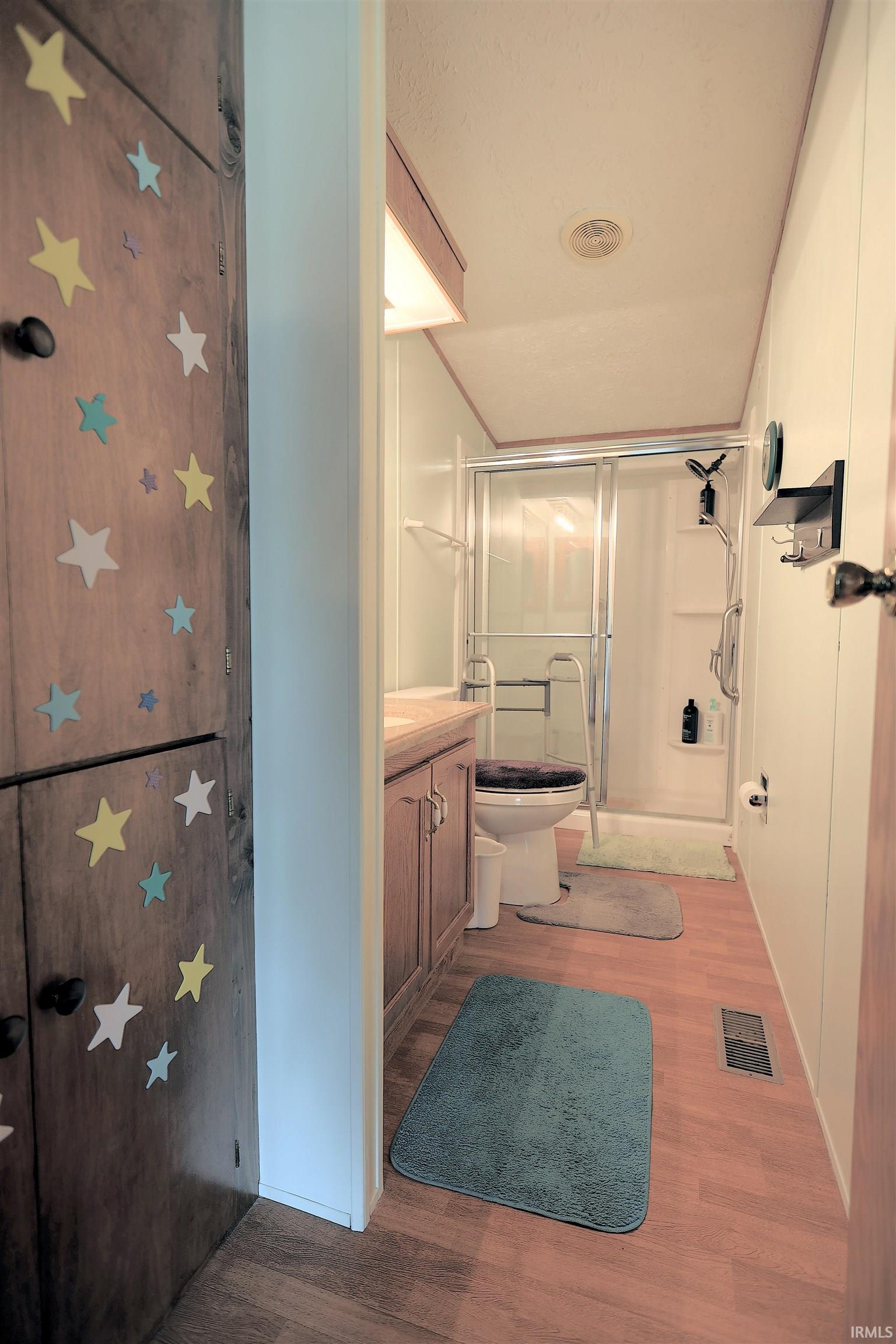 Bathroom featuring a stall shower with sliding glass doors, a vanity with wood-finish cabinetry, and wood-finish flooring