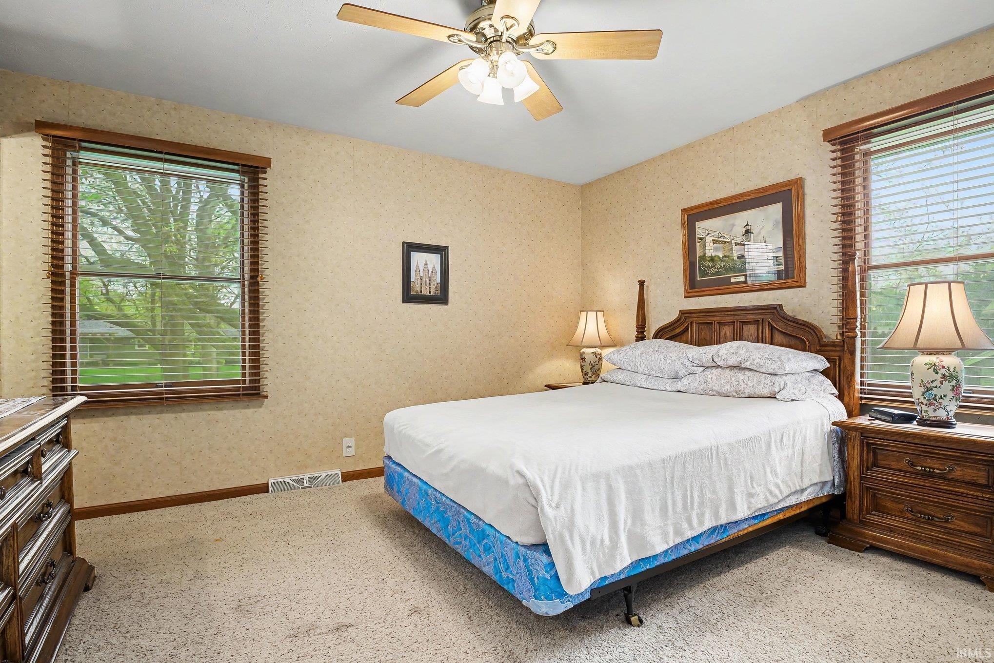 Carpeted room featuring dual windows with wood-finish blinds and trim, textured wall covering, and a ceiling fan with light fixture