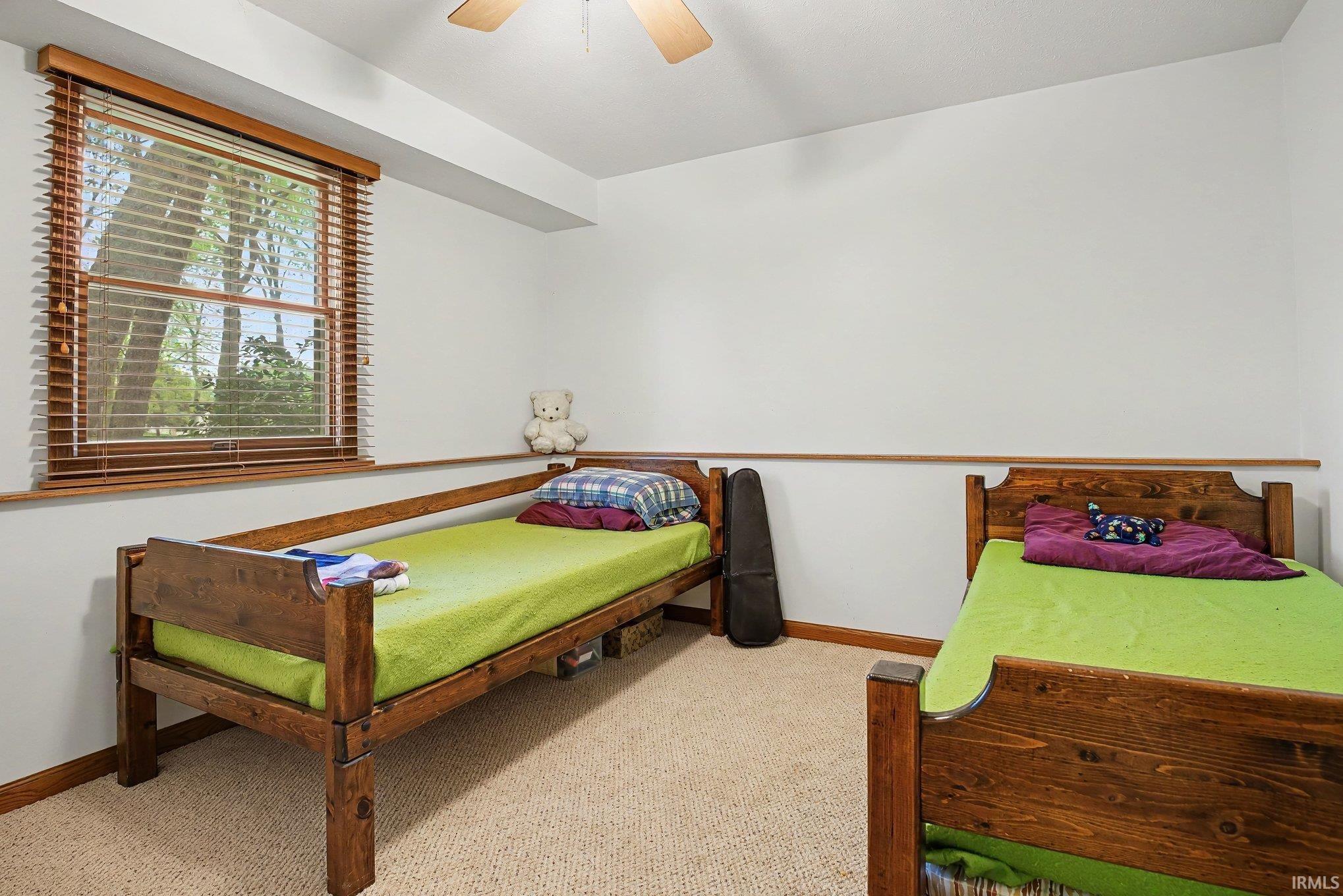 Carpeted room with a ceiling fan, a window featuring wood-tone blinds, and white walls with a wood-tone chair rail