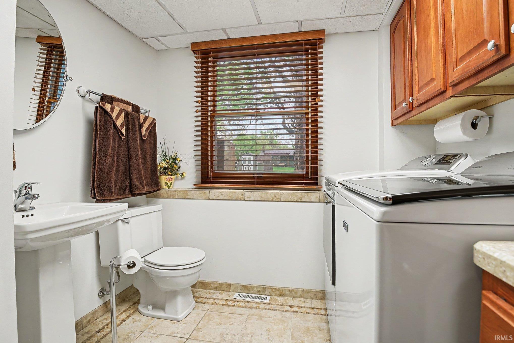 Combined laundry and powder room featuring a pedestal sink, toilet, window with wood-finish blinds, and tile flooring