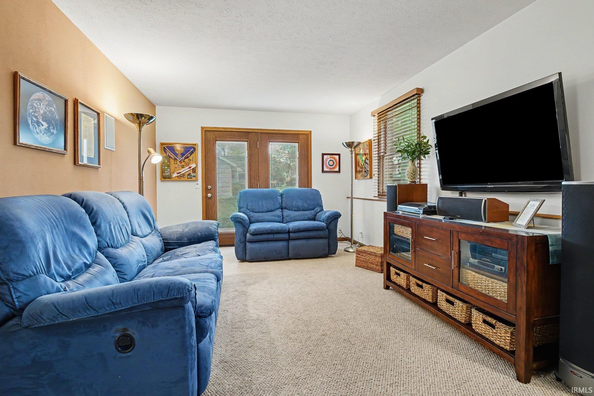 Carpeted living area featuring a neutral color palette, dual-pane glass patio doors, and a built-in media console with glass-front cabinets