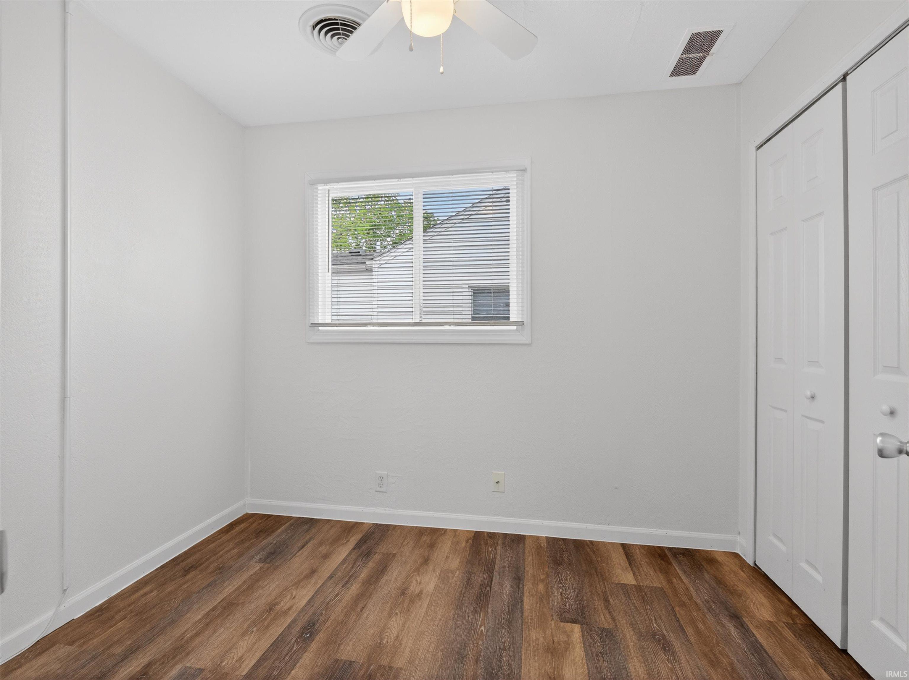 Room with wood-finish flooring, white walls, and a window with blinds