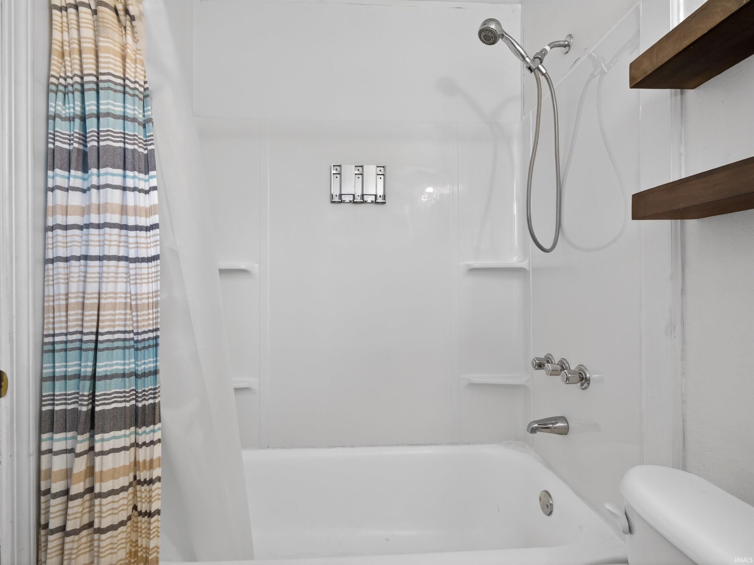 Bathtub and shower combination featuring a white surround, built-in shelving, and chrome fixtures