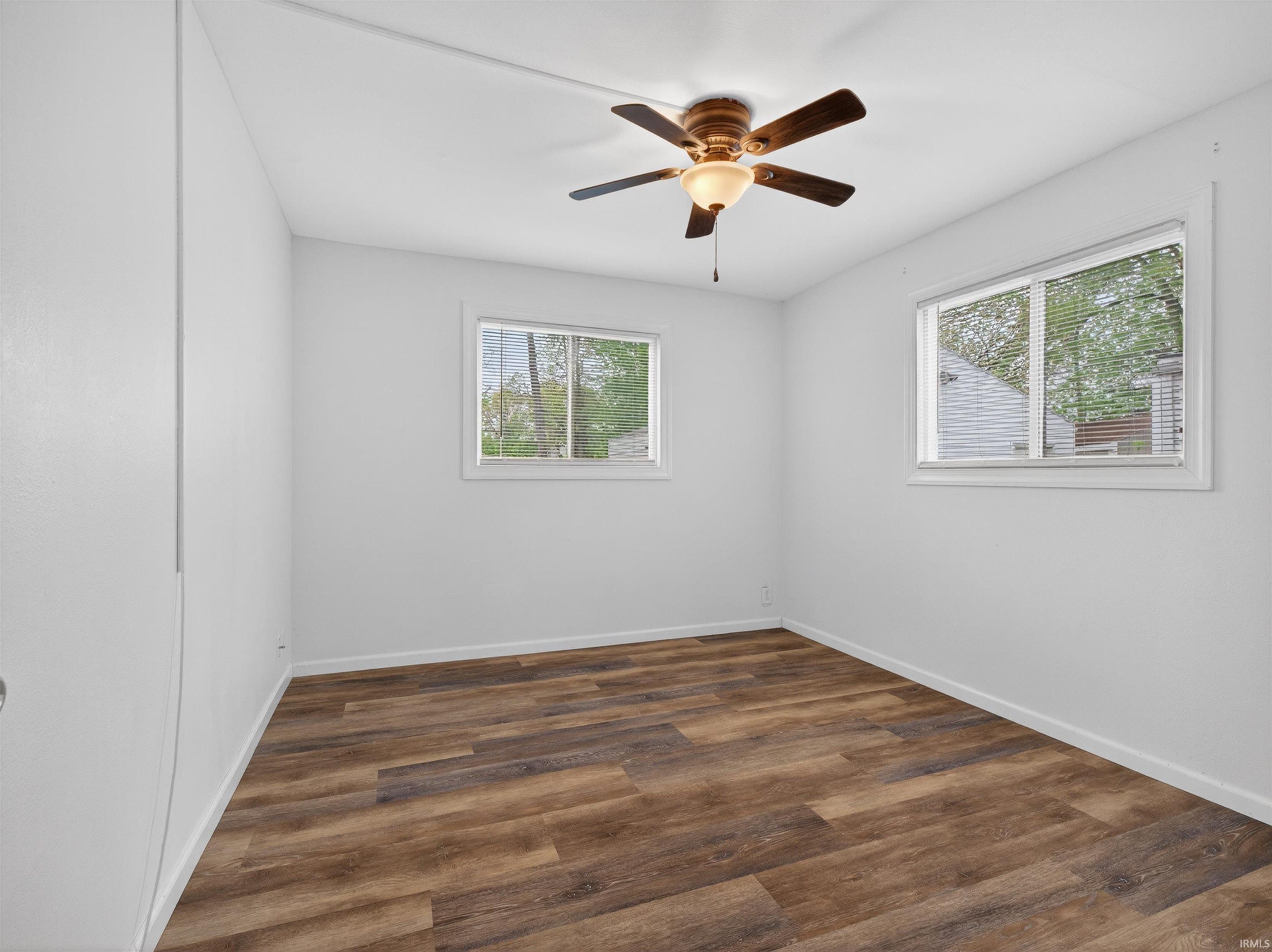 Spacious room featuring wood-finish flooring, white walls, and a ceiling fan with integrated lighting