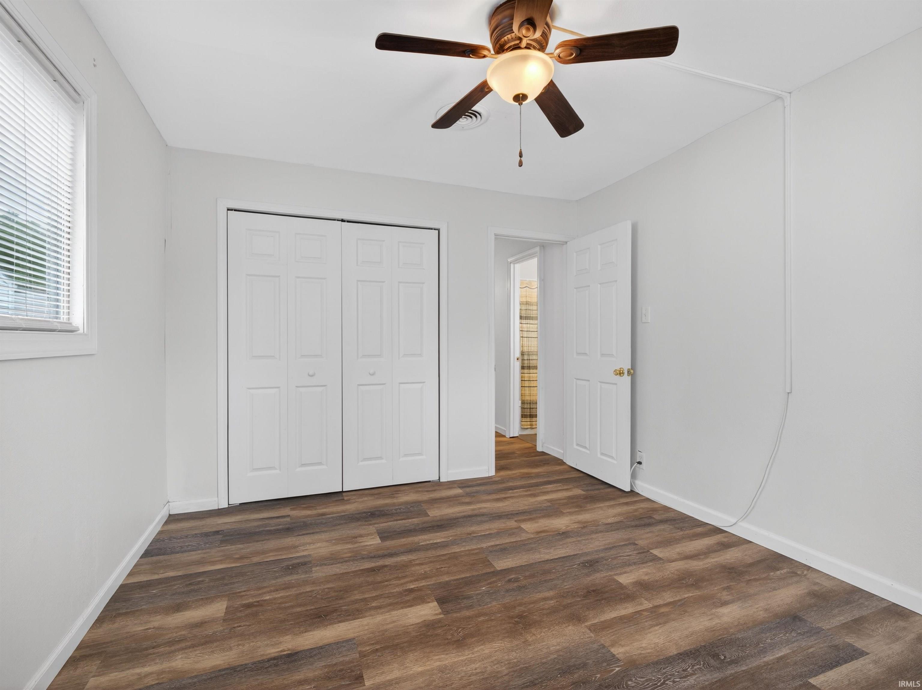 Neutral-toned room with wood-finish flooring, white walls, and a ceiling fan with integrated lighting