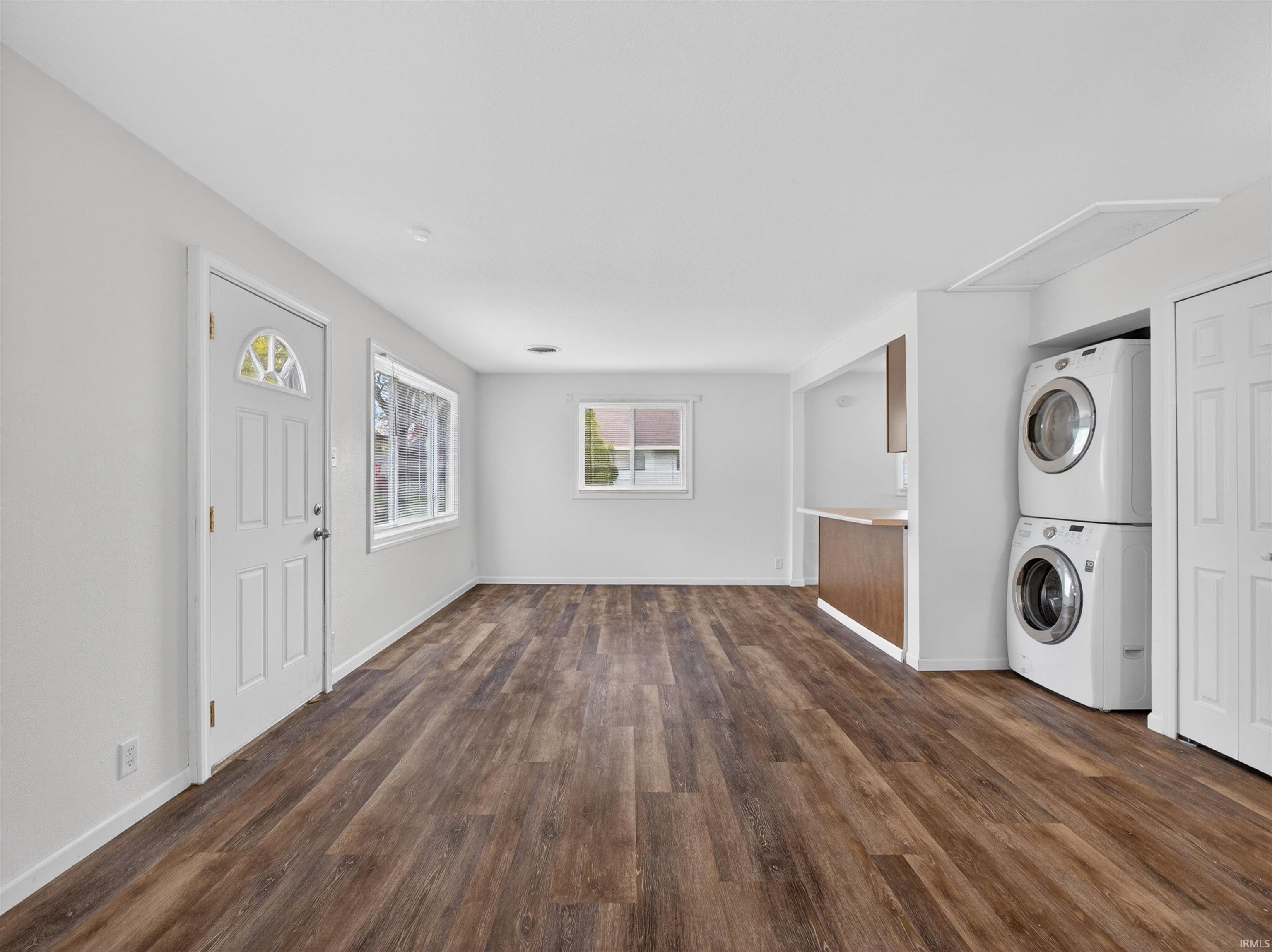 Expansive room featuring wood-finish flooring, white walls, and a white entry door with an arched glass insert