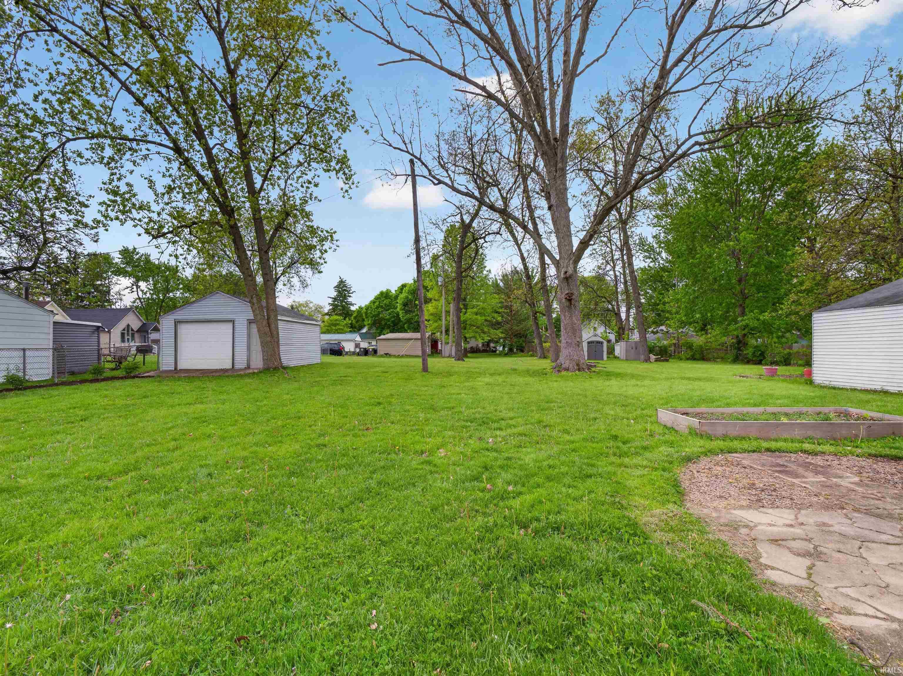 Expansive green lawn with mature trees and a detached garage featuring a white overhead door