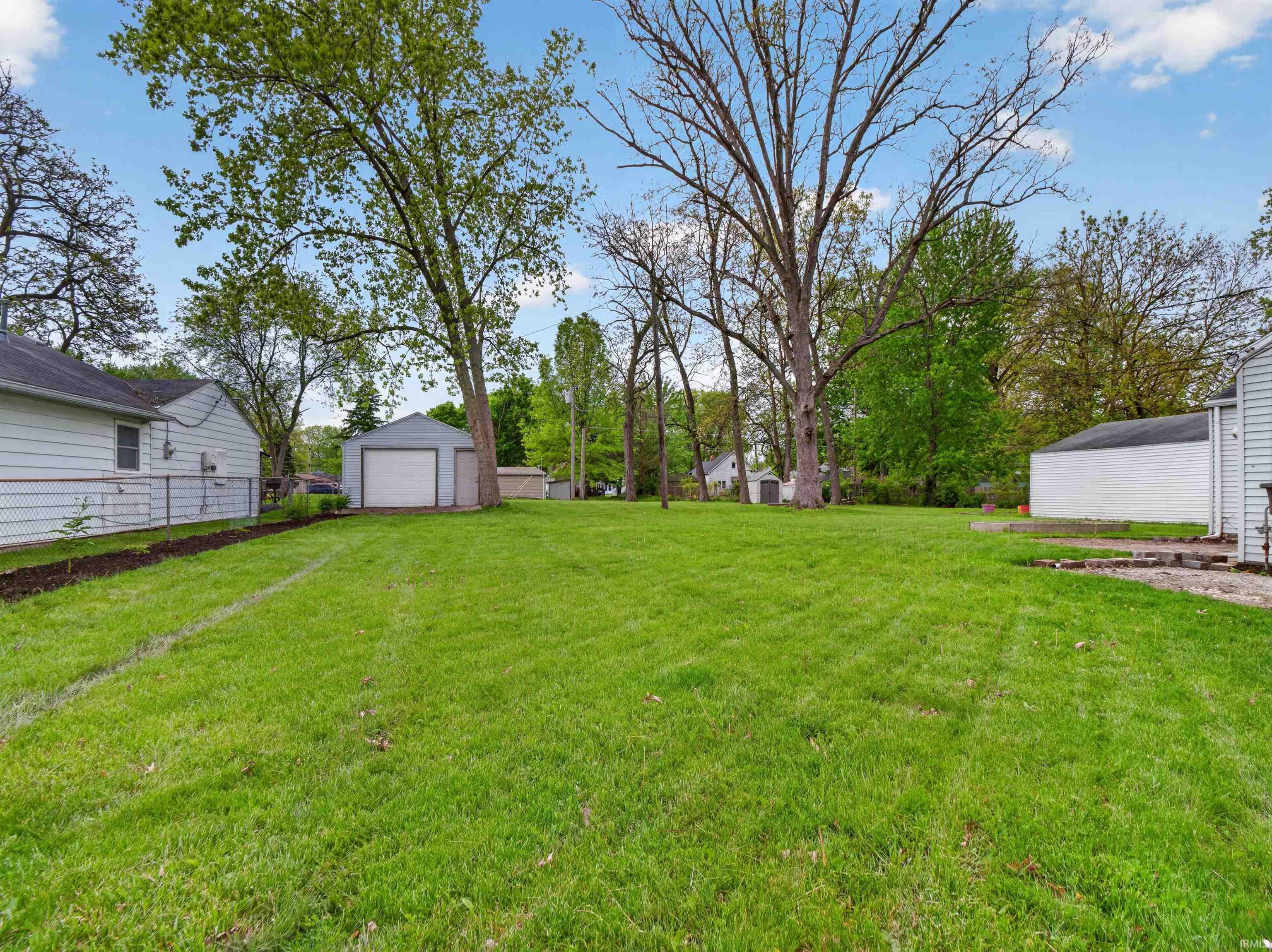 Expansive green lawn with mature trees and a detached garage featuring a white overhead door