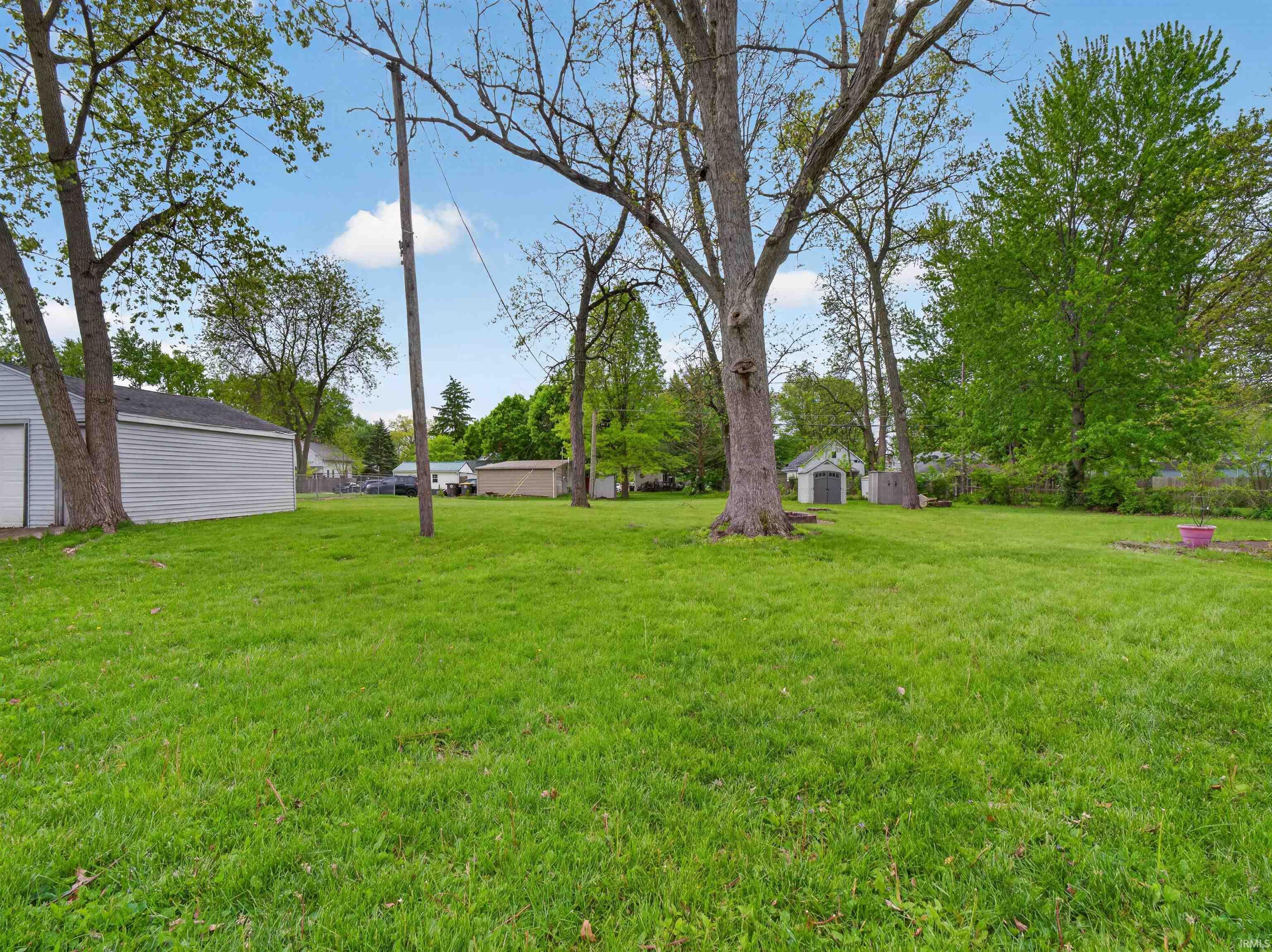 Expansive grassy yard featuring mature trees and a detached garage with white siding