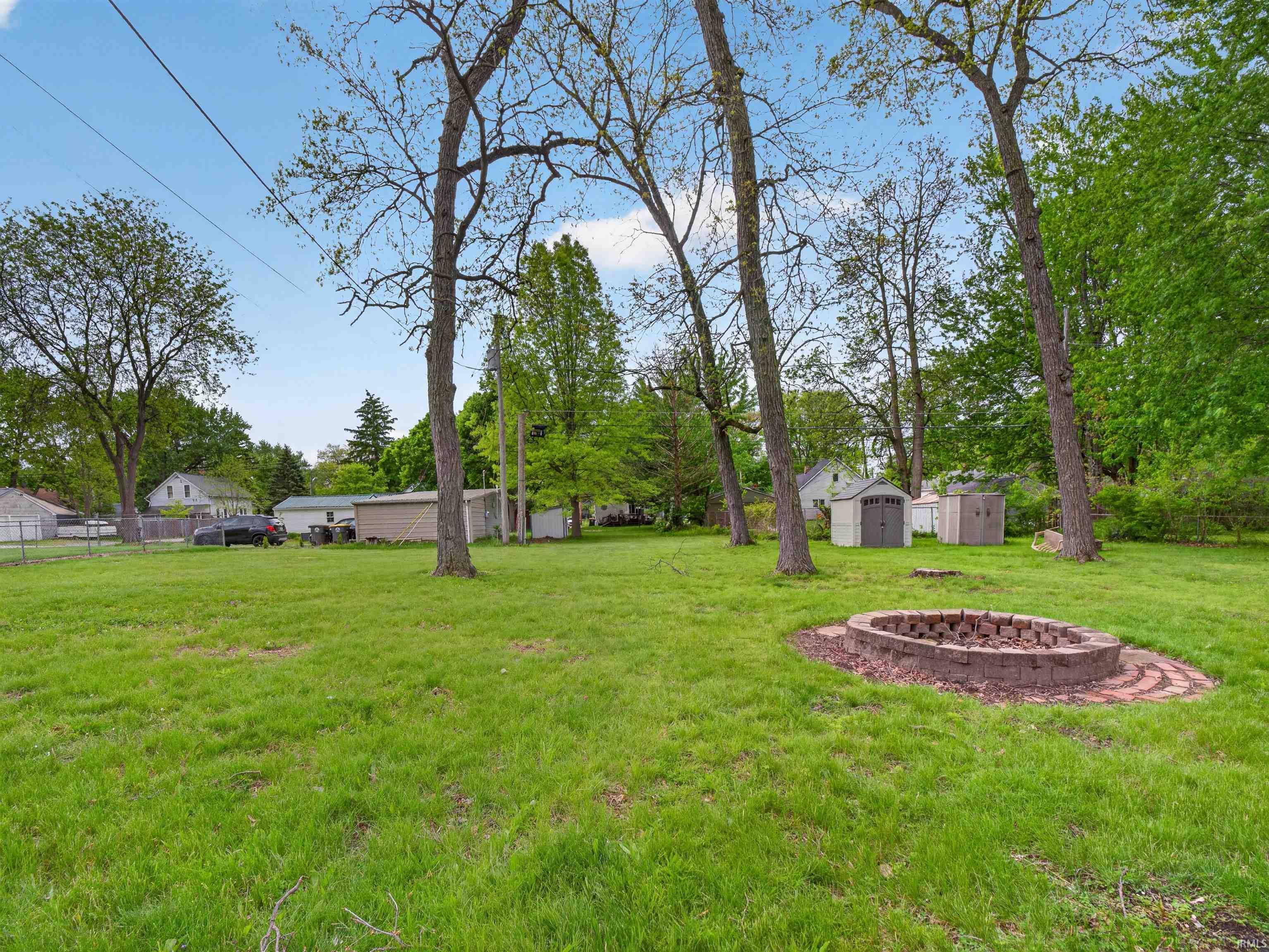 Expansive green lawn featuring mature trees and a built-in stone fire pit with brick detailing