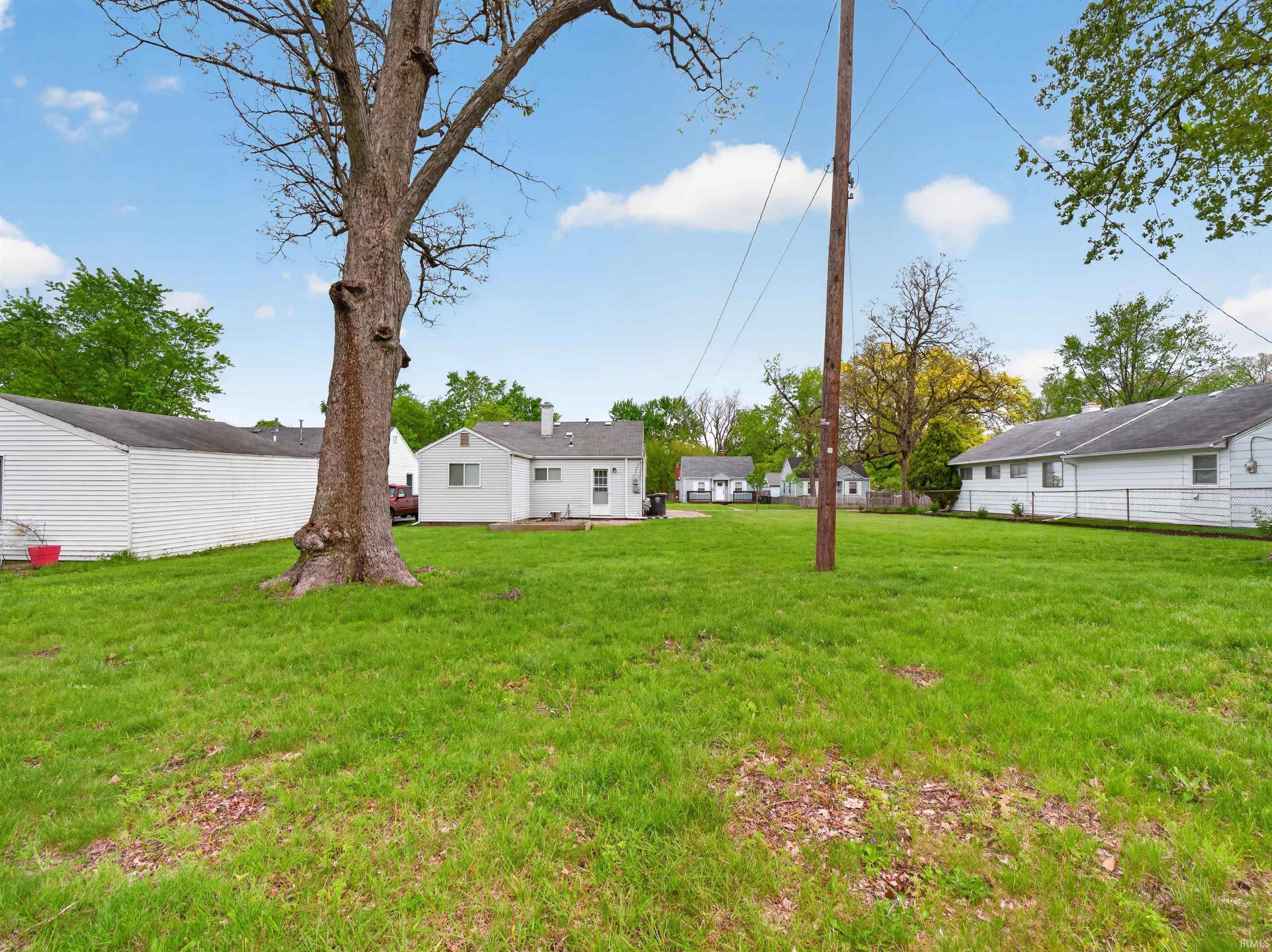 Expansive green lawn with mature tree, bordered by white siding structures