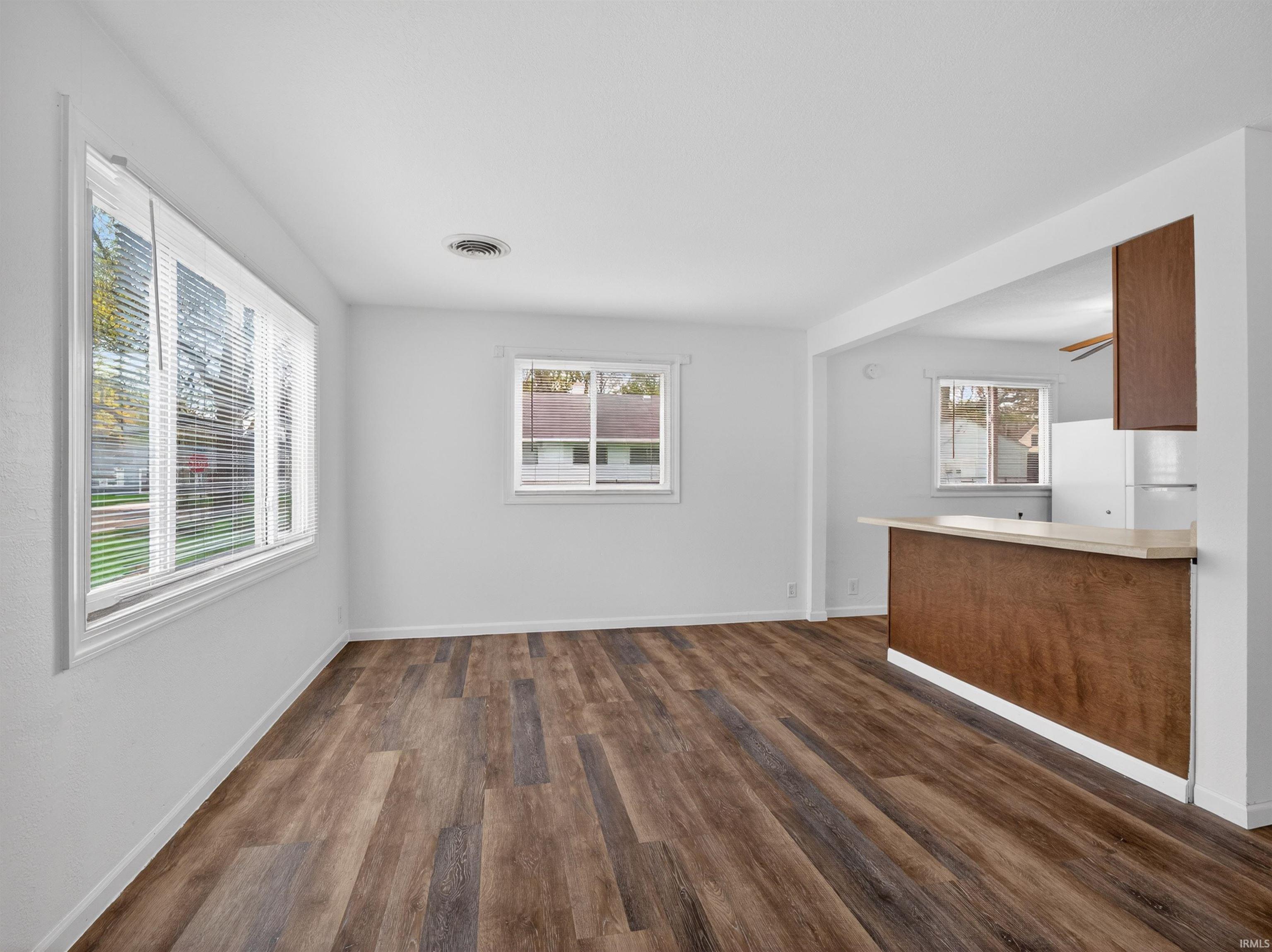 Spacious room featuring wood-finish flooring, white walls, and multiple windows with blinds
