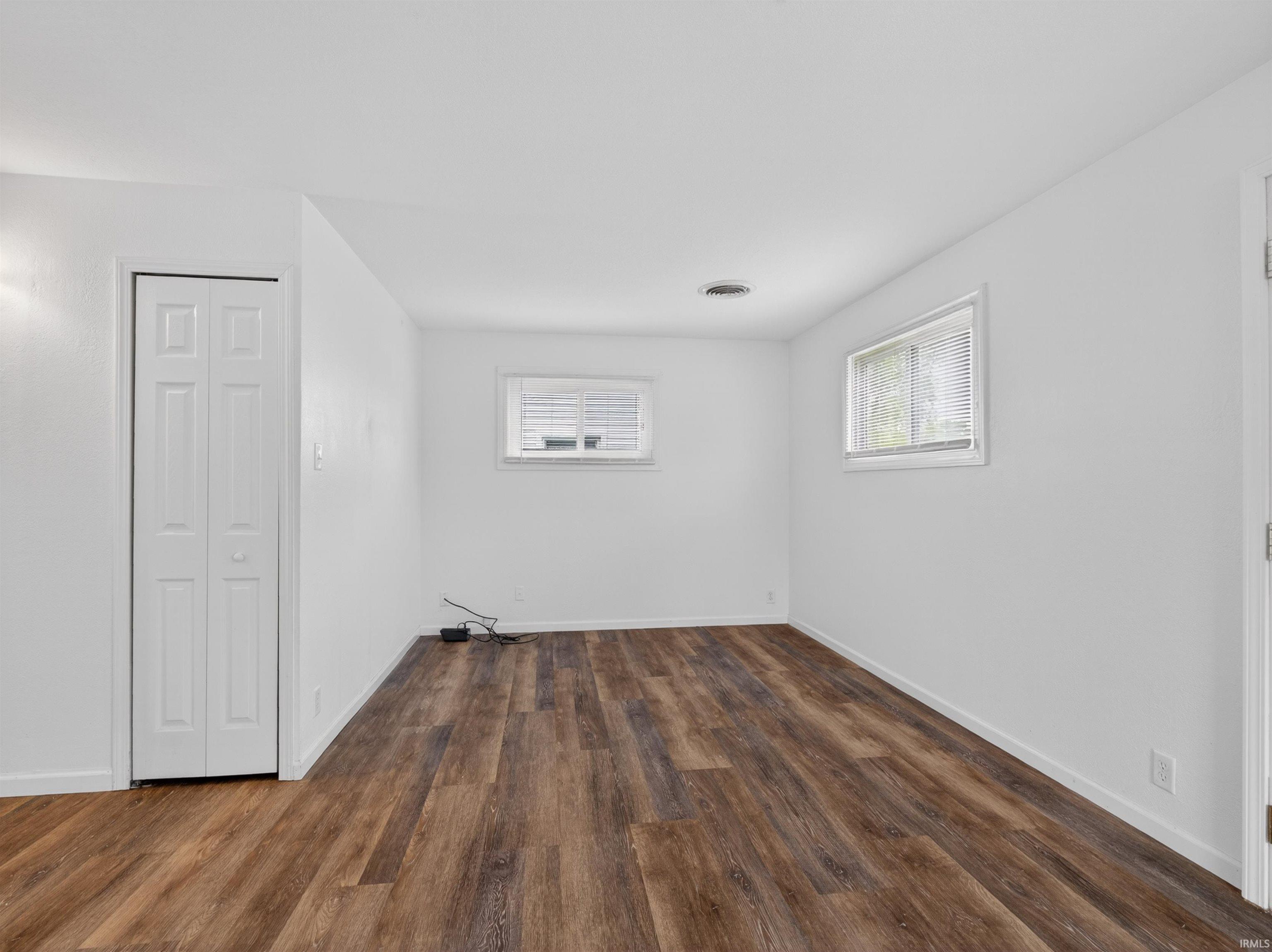 Spacious room featuring wood-finish flooring, white walls, and two windows with blinds