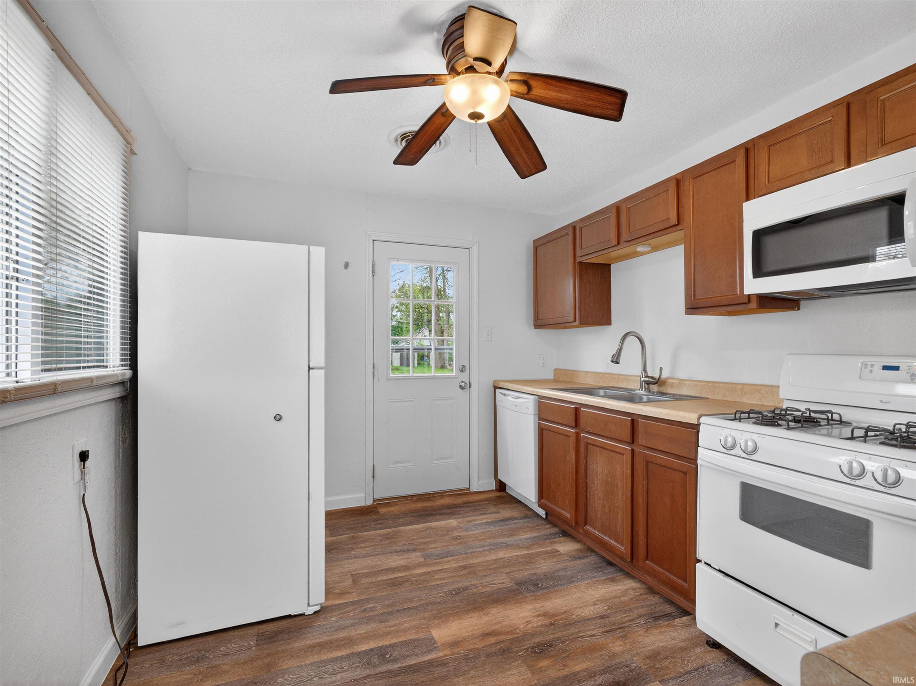 Kitchen featuring wood-finish flooring, wood cabinetry, built-in microwave, white refrigerator, and a ceiling fan with integrated lighting