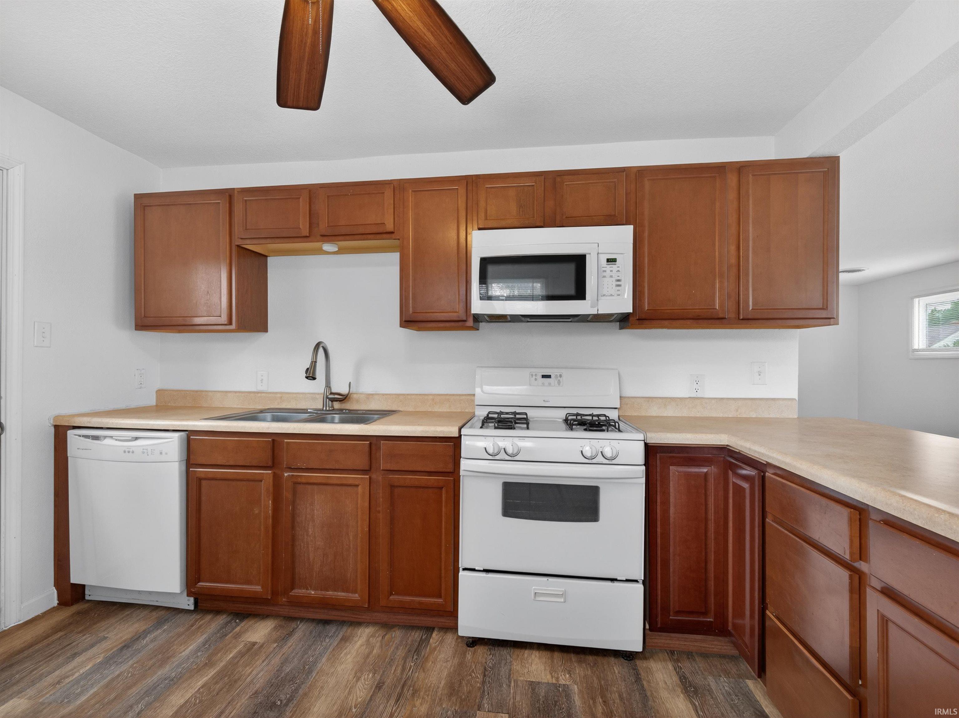 Kitchen featuring rich wood cabinetry, light-toned countertops, wood-finish flooring, a white gas range, and a built-in microwave