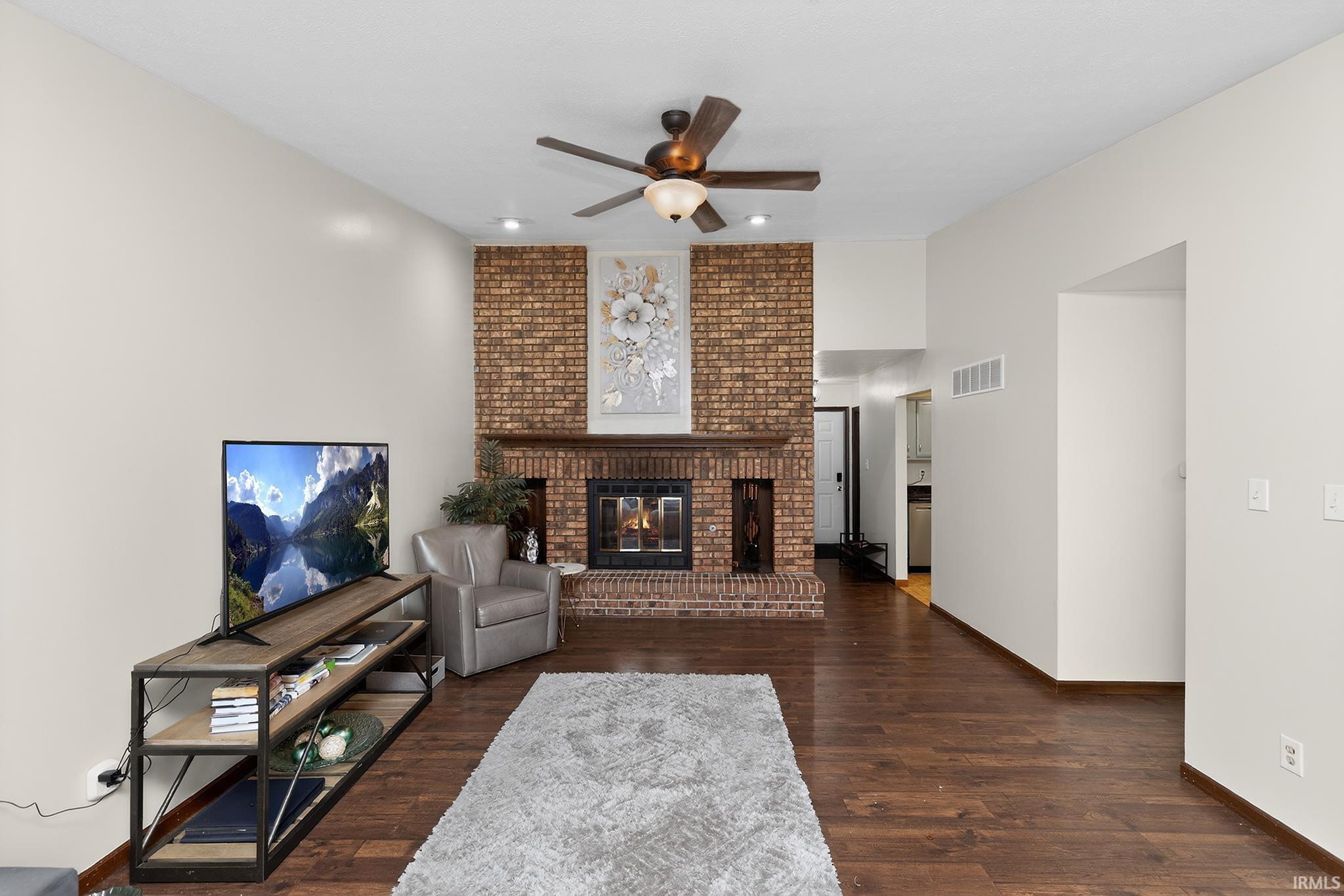 Living area featuring a floor-to-ceiling brick fireplace with a wood mantel, wood-finish flooring, and a ceiling fan with integrated lighting