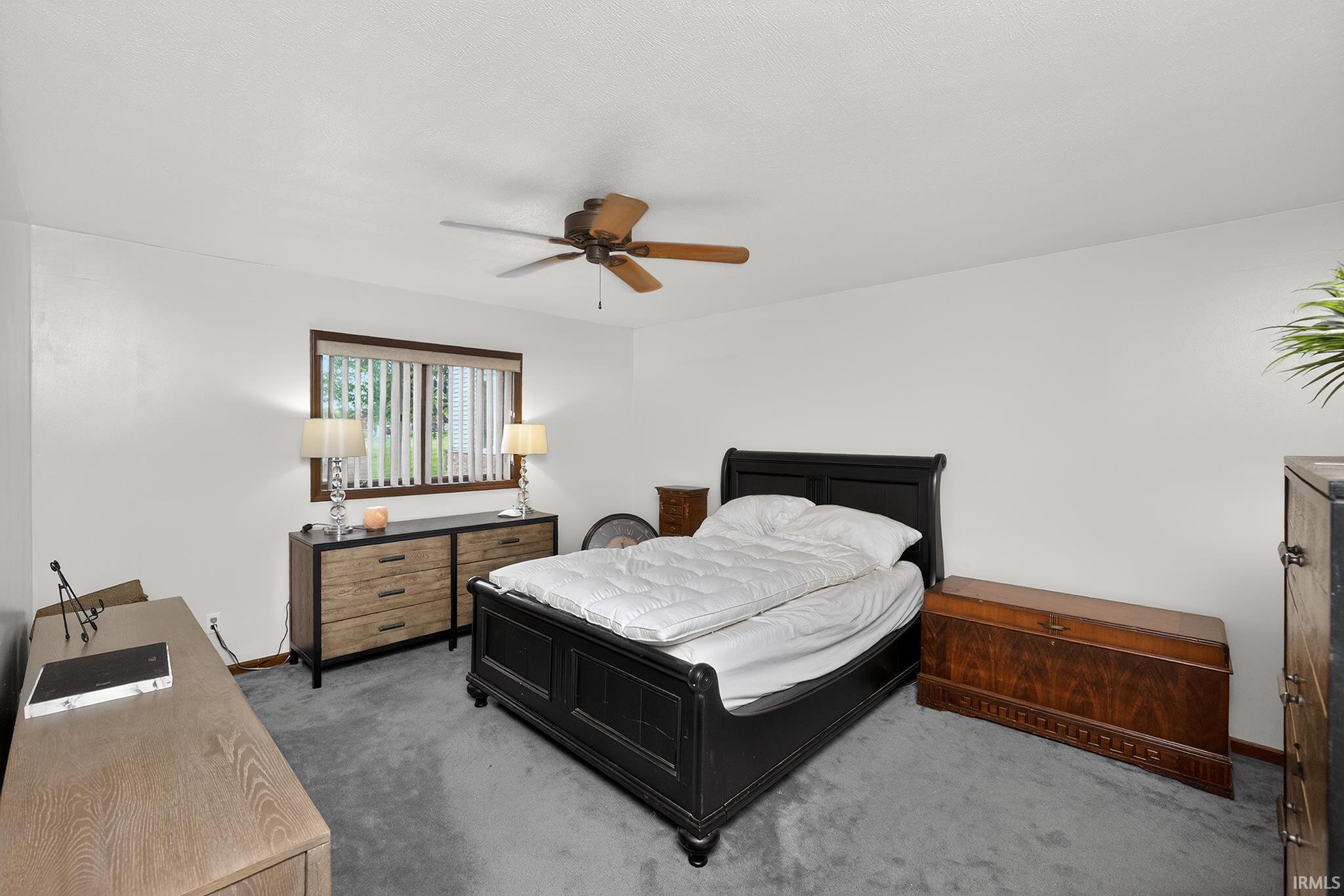 Carpeted bedroom featuring a ceiling fan, a window with vertical blinds, and white walls