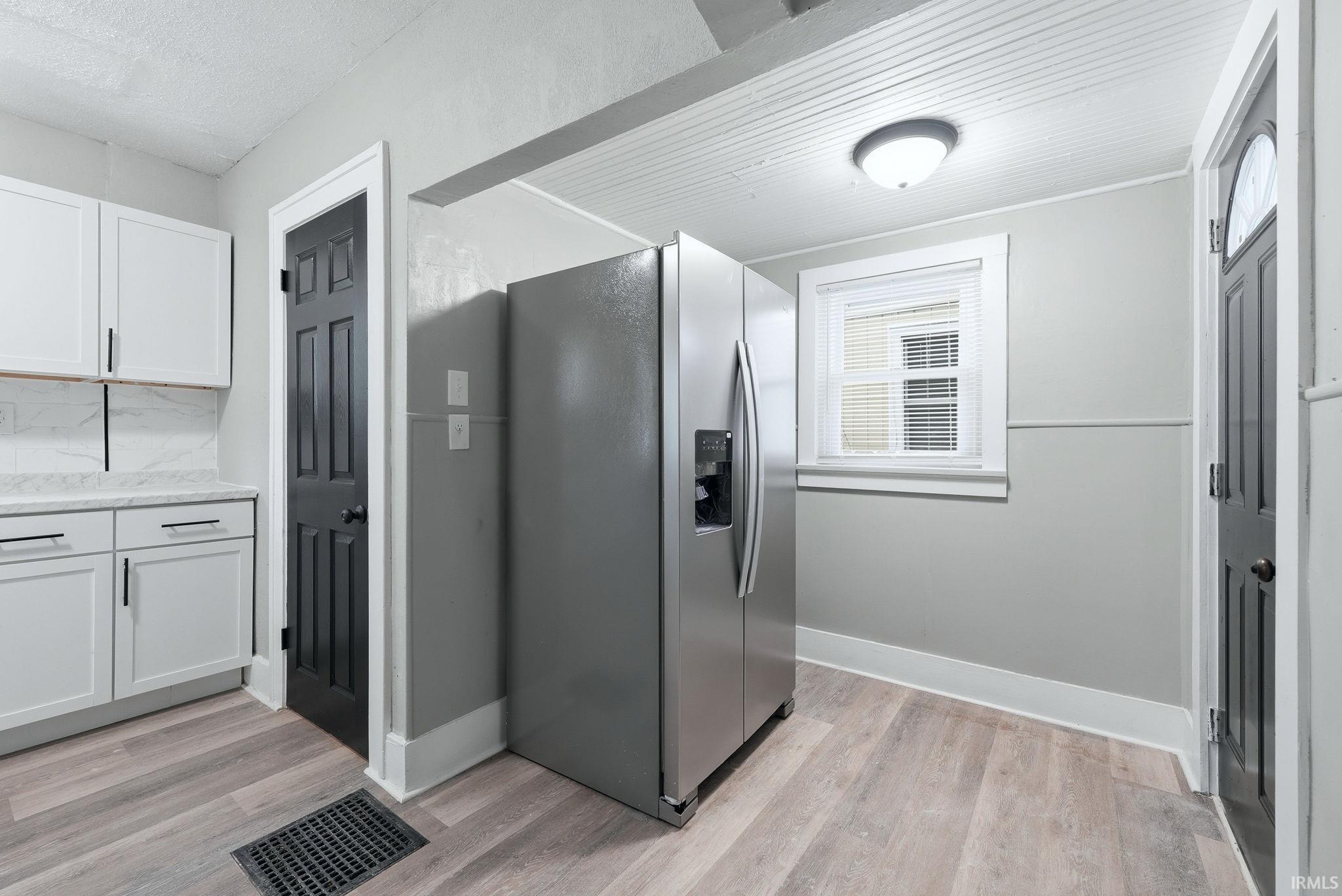 Kitchen featuring wood-finish flooring, white cabinetry with black hardware, and a stainless steel side-by-side refrigerator
