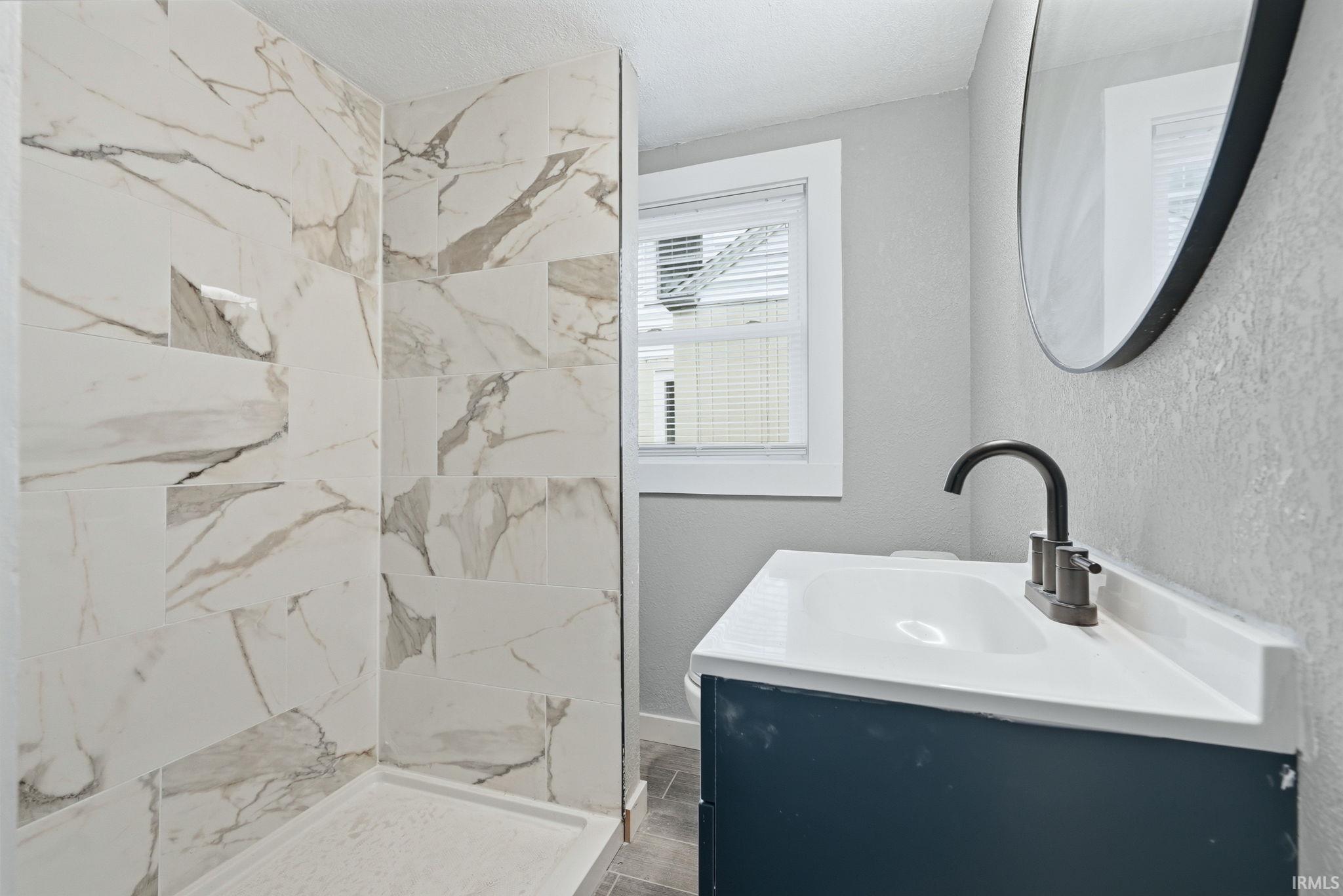 Shower with large-format white and grey veined wall tile, an integrated shower niche, and a white shower pan