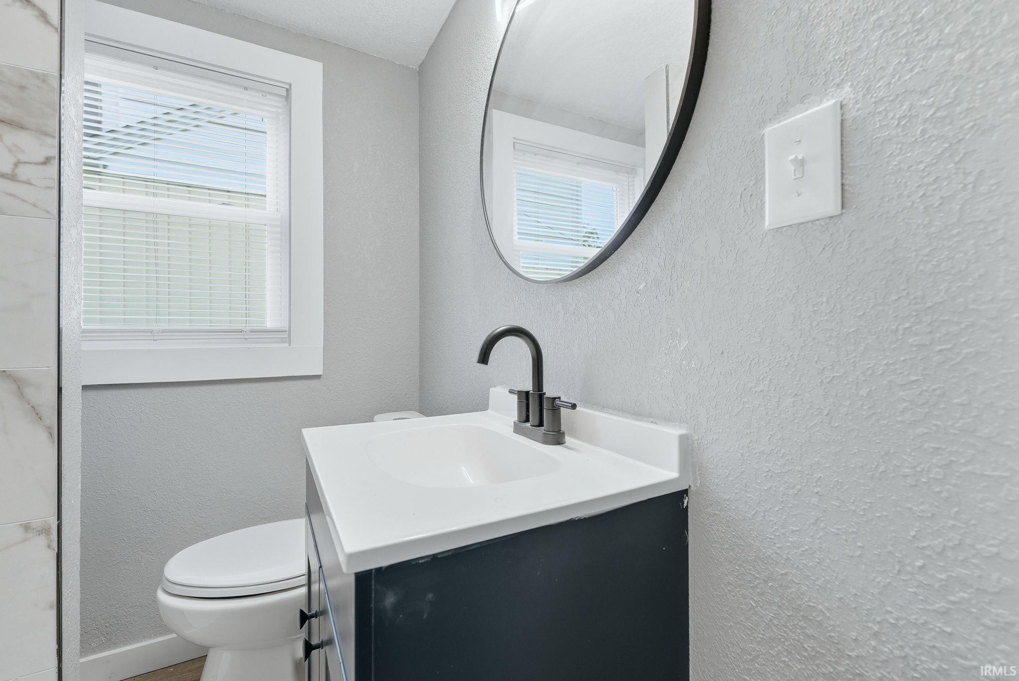 Bathroom featuring a dark vanity with white countertop and integrated sink, a matte black faucet, and a round wall-mounted mirror