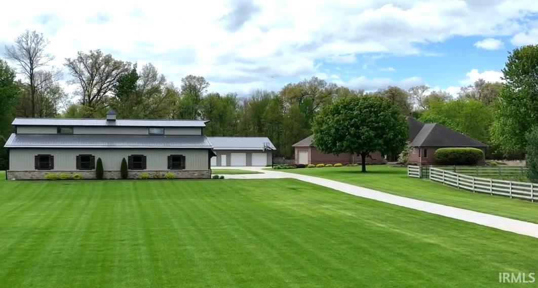 Expansive green lawn with a long concrete driveway leading to a multi-bay garage and a separate structure with a metal roof and stone accents