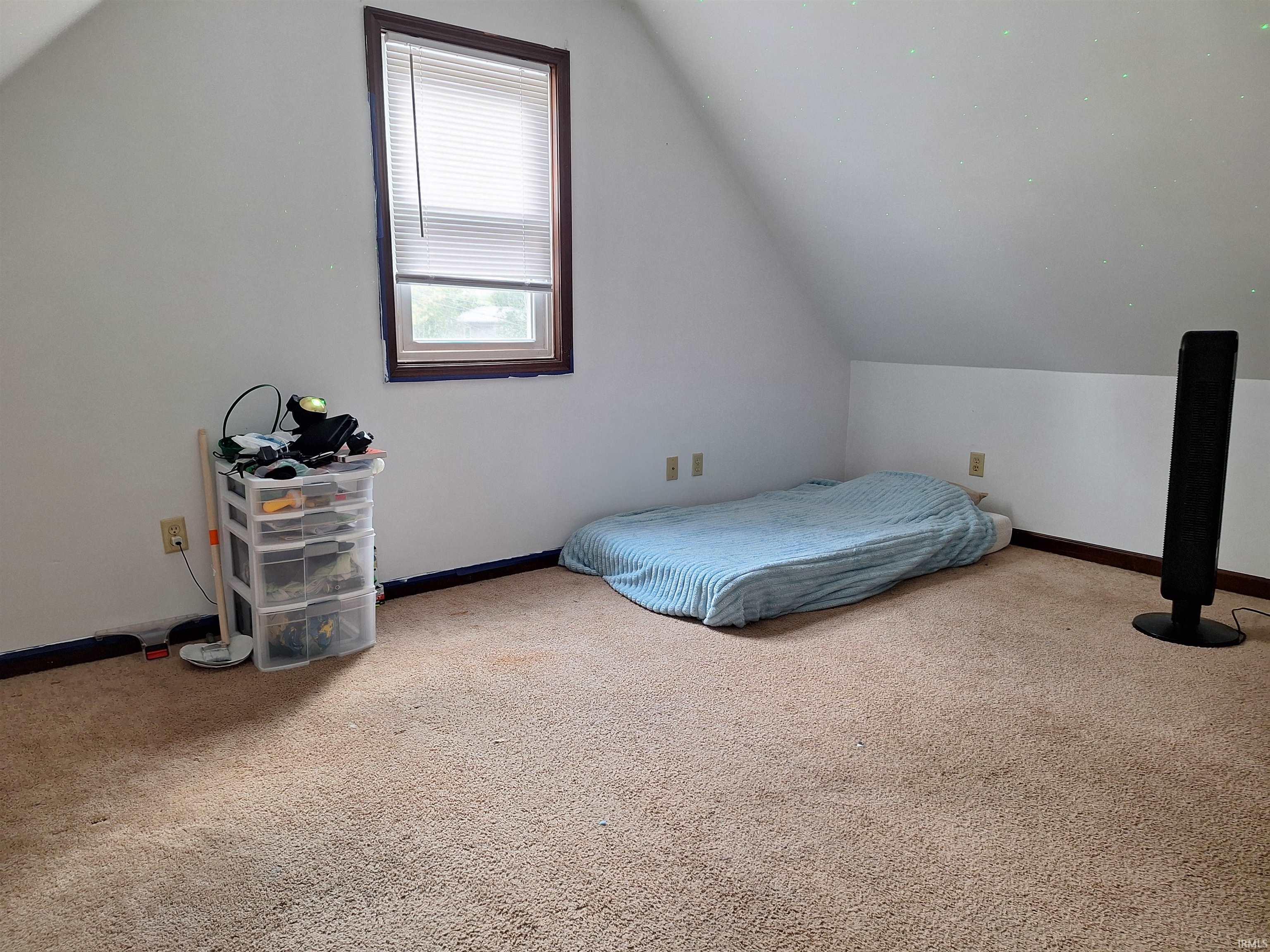 Attic space featuring sloped ceilings, a single window with blinds, and light-colored carpet flooring