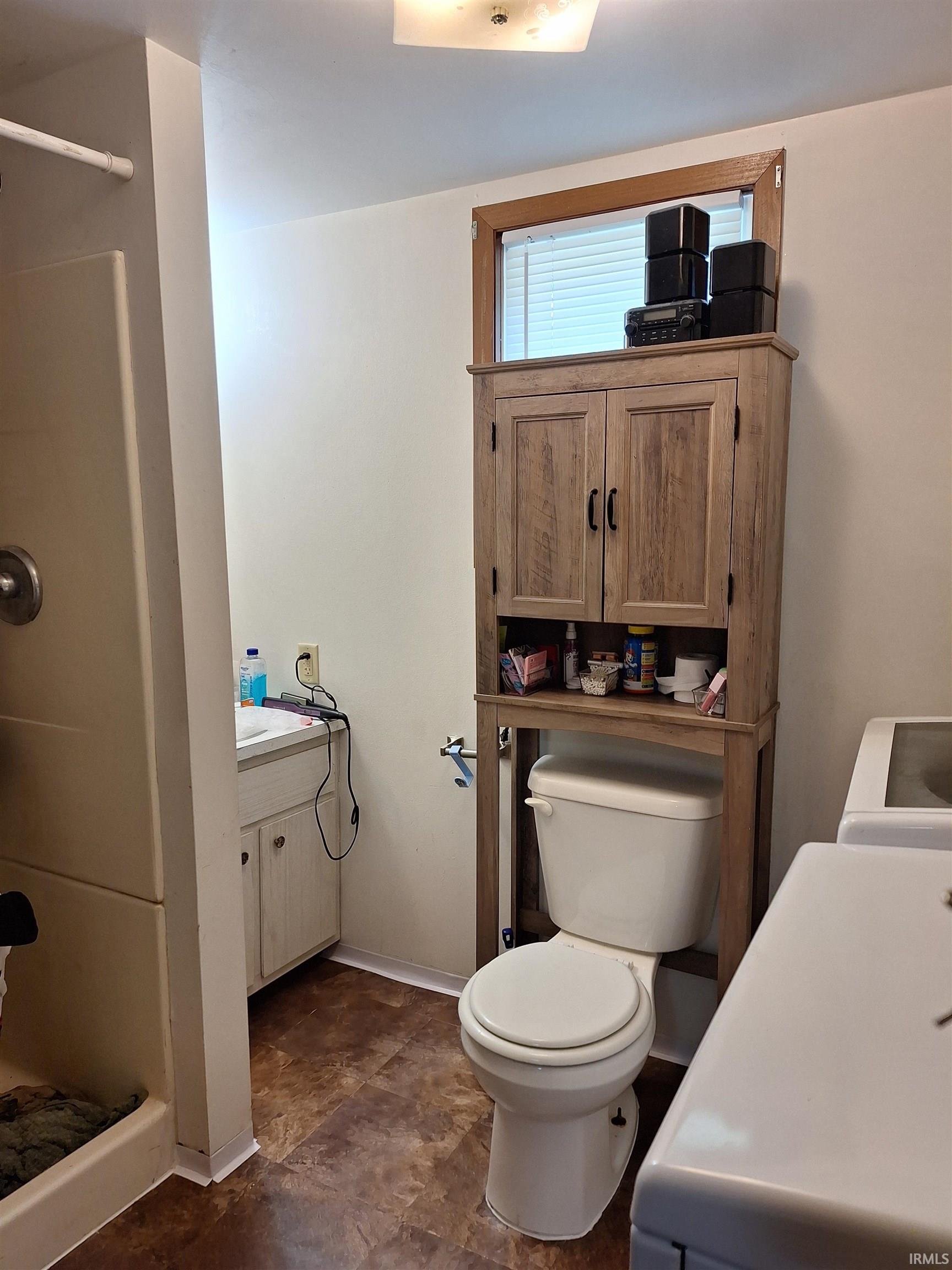 Bathroom featuring a shower stall, a vanity with a white countertop and base cabinetry, a toilet with an over-the-toilet storage cabinet, and vinyl flooring