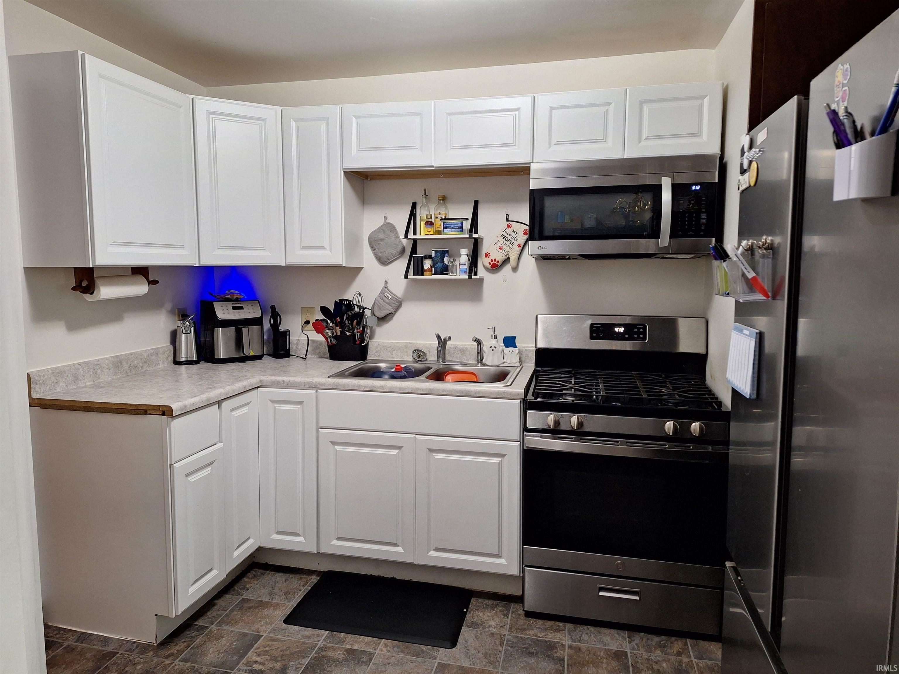 Modern kitchen featuring white shaker-style cabinetry, L-shaped laminate countertops, a stainless steel gas range, and a coordinating over-the-range microwave