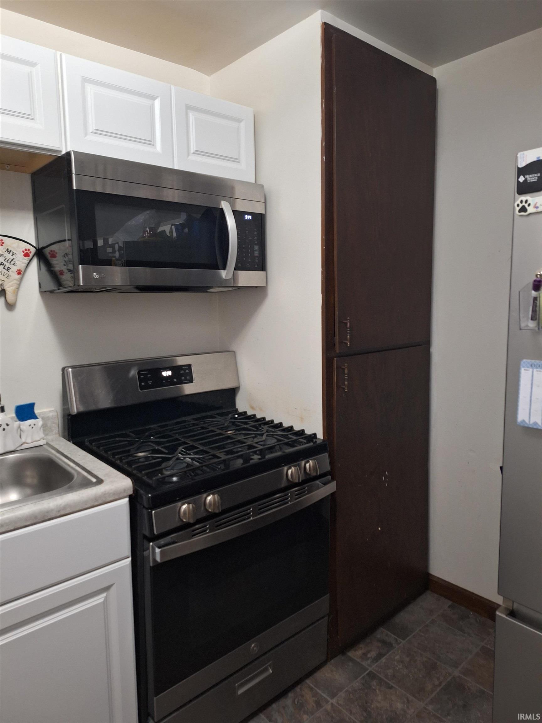 Modern stainless steel range with overhead microwave, white upper and lower cabinetry, and a stainless steel sink