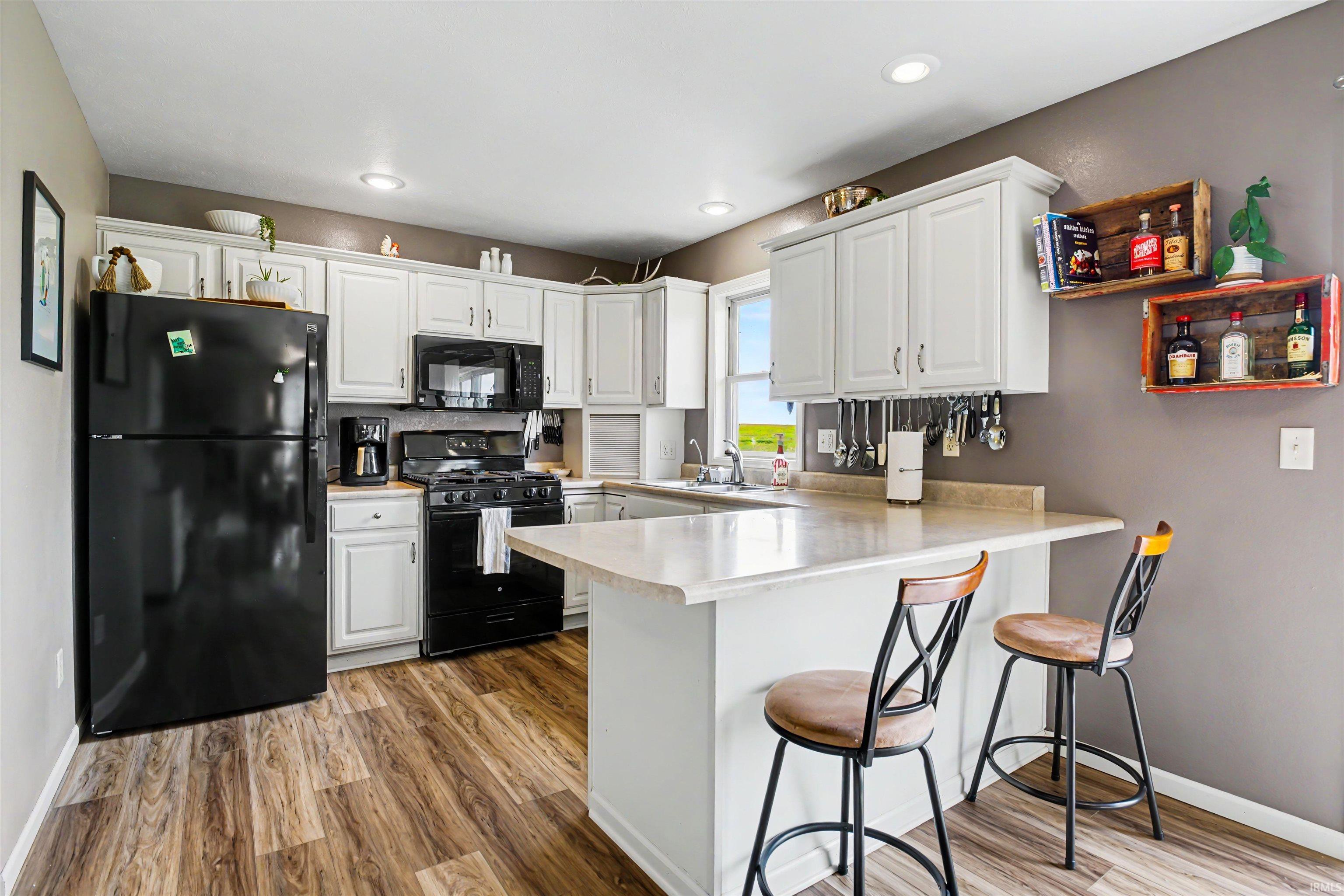 Kitchen featuring wood-finish flooring, white cabinetry with silver-tone hardware, a light-toned countertop, recessed lighting, and a black appliance suite