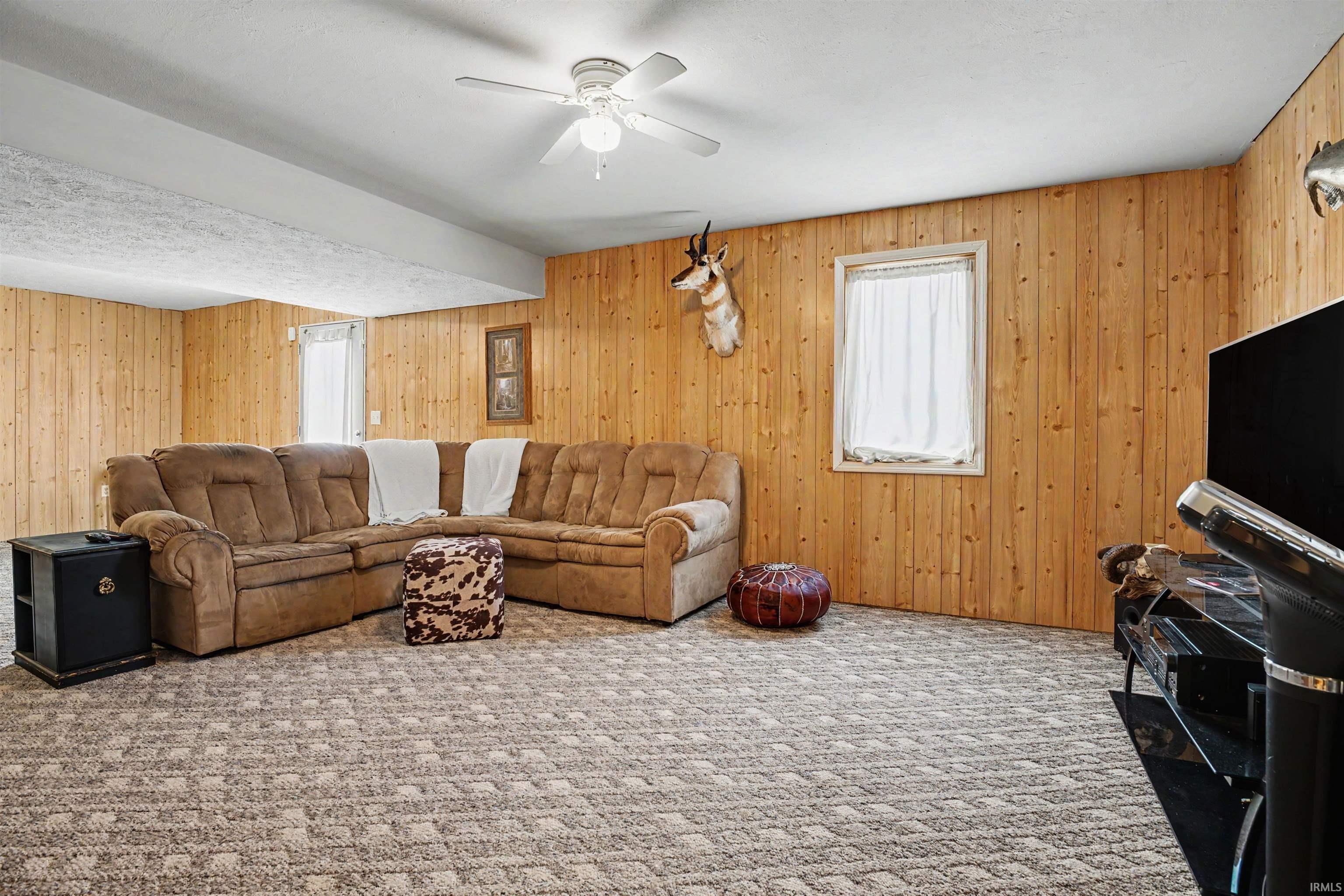 Spacious room featuring wood paneling throughout, a patterned carpet, and a ceiling fan with integrated lighting